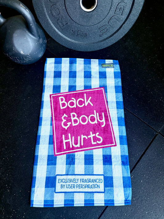 Blue and white checkered towel with 'Back & Body Hurts' text on a dark surface with gym equipment.