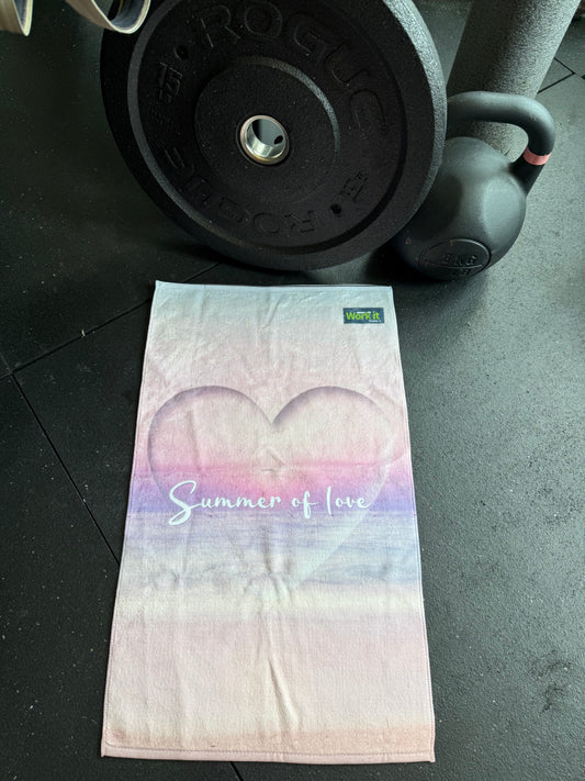 Towel with heart design and text on a gym floor next to a barbell