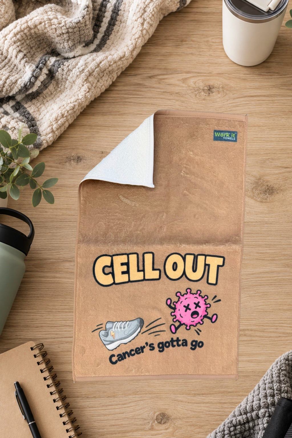 Tan Cell Out towel with one corner folded back to show the soft white terry backing, on a wood table with a blanket and drinkware.