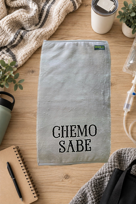 grey plush towel with 'chemo sabe' in black font on a hardwood floor with blankets and drinks