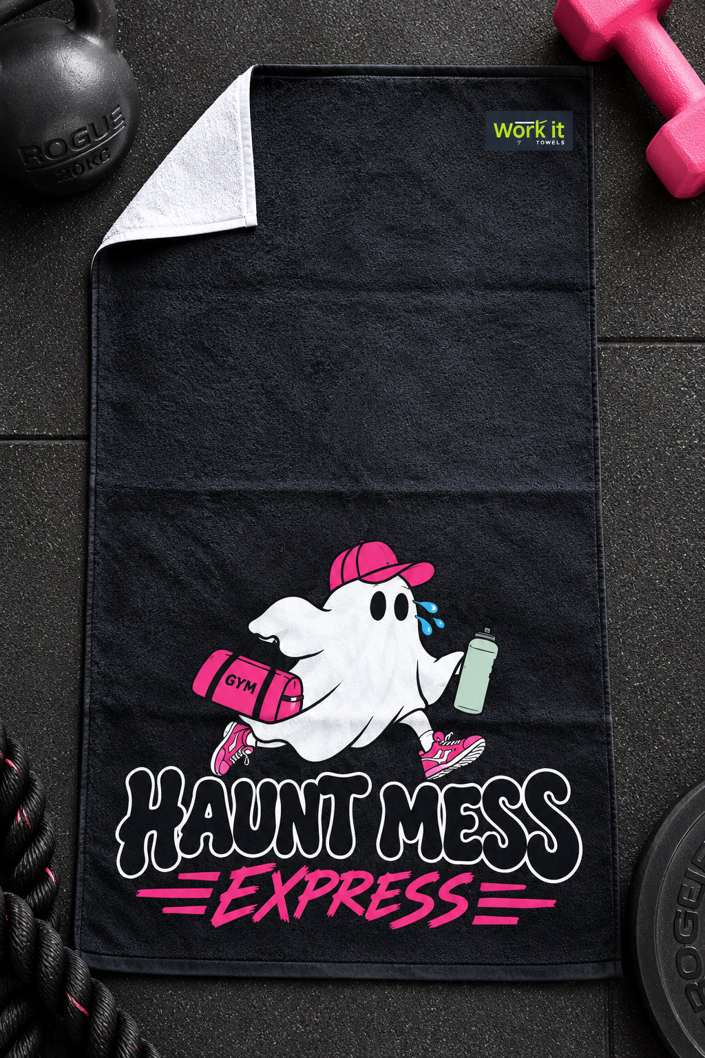 A black gym towel laid flat on a dark textured surface, featuring a cartoon ghost running with a pink backpack and holding a green water bottle. The text 'HAUNT MESS EXPRESS' is printed in white and pink below the ghost.