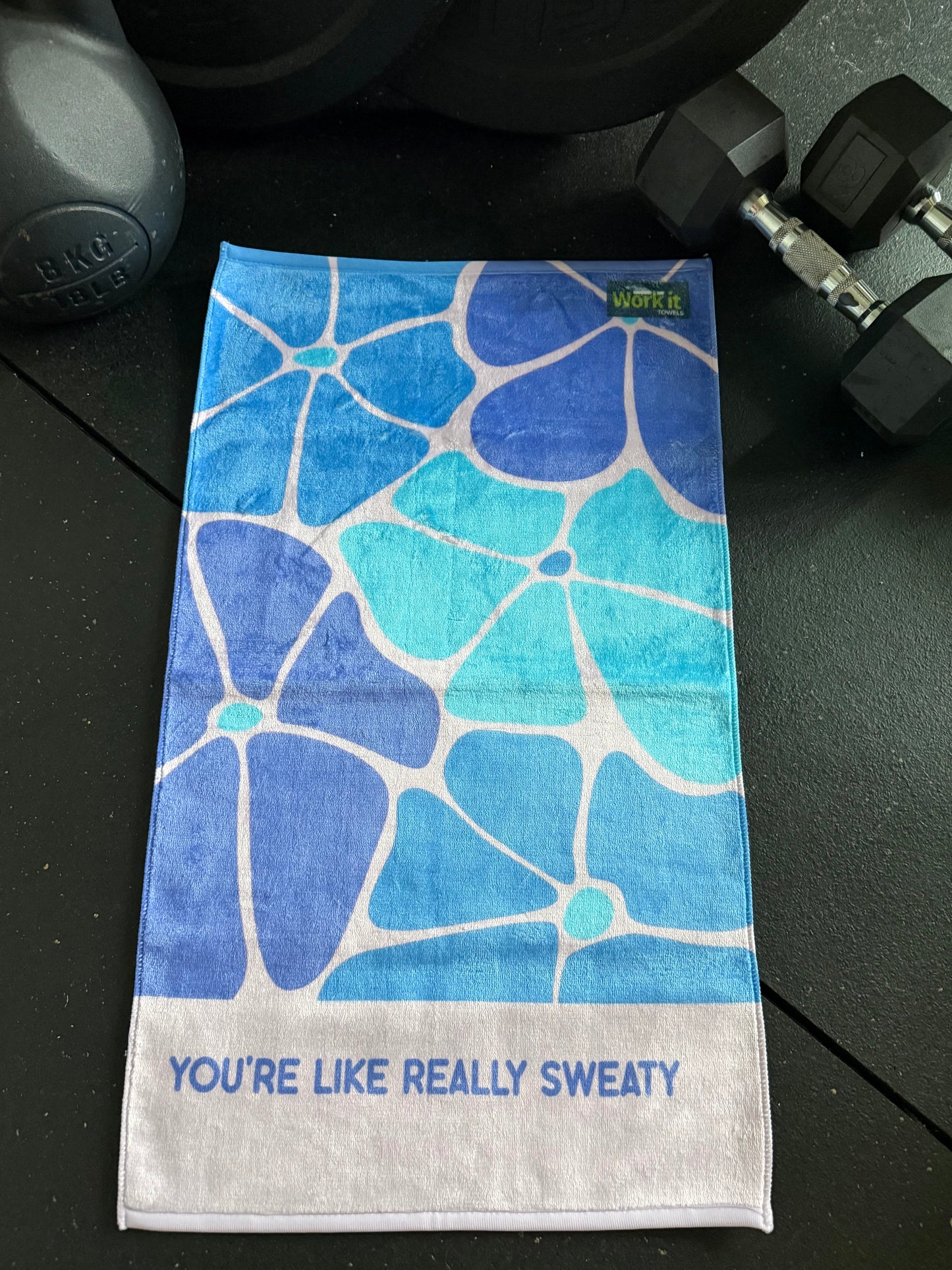 Blue floral patterned towel with text on a black surface with dumbbells