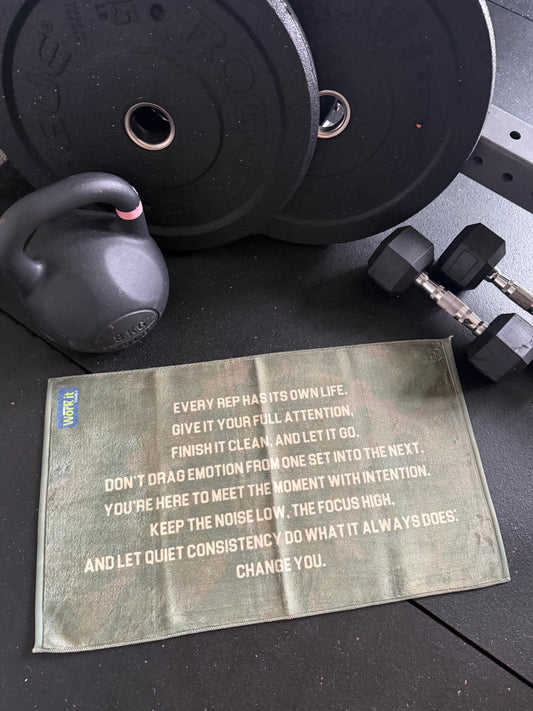 Motivational towel on a gym floor with weights and dumbbells in the background