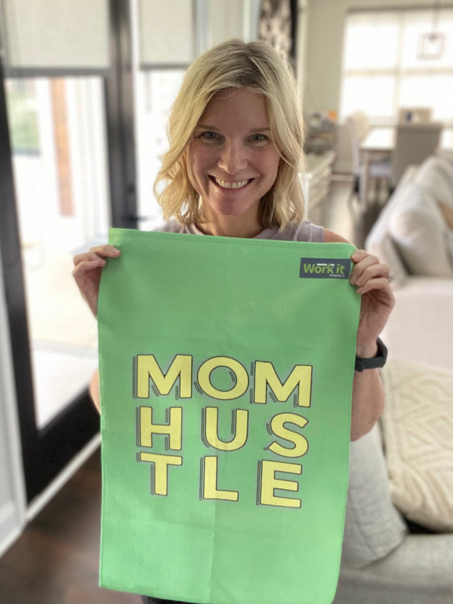 Woman holding a green gym towel with 'Mom Hustle' text