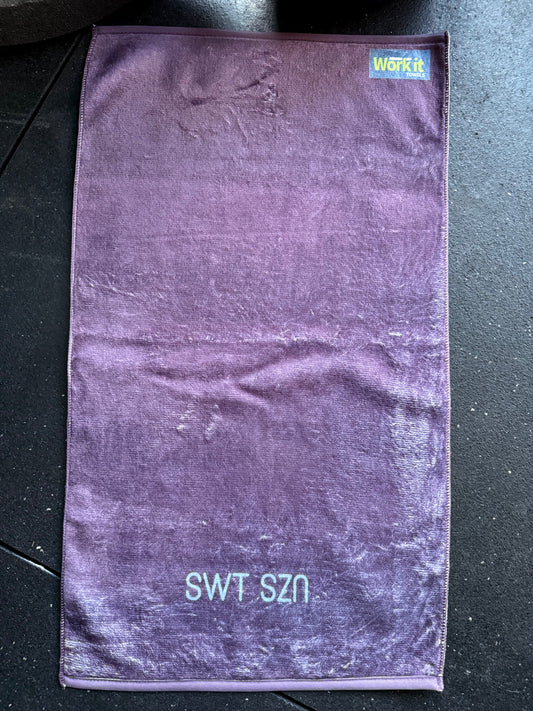 Purple towel with 'SWT SZN' text on a black surface