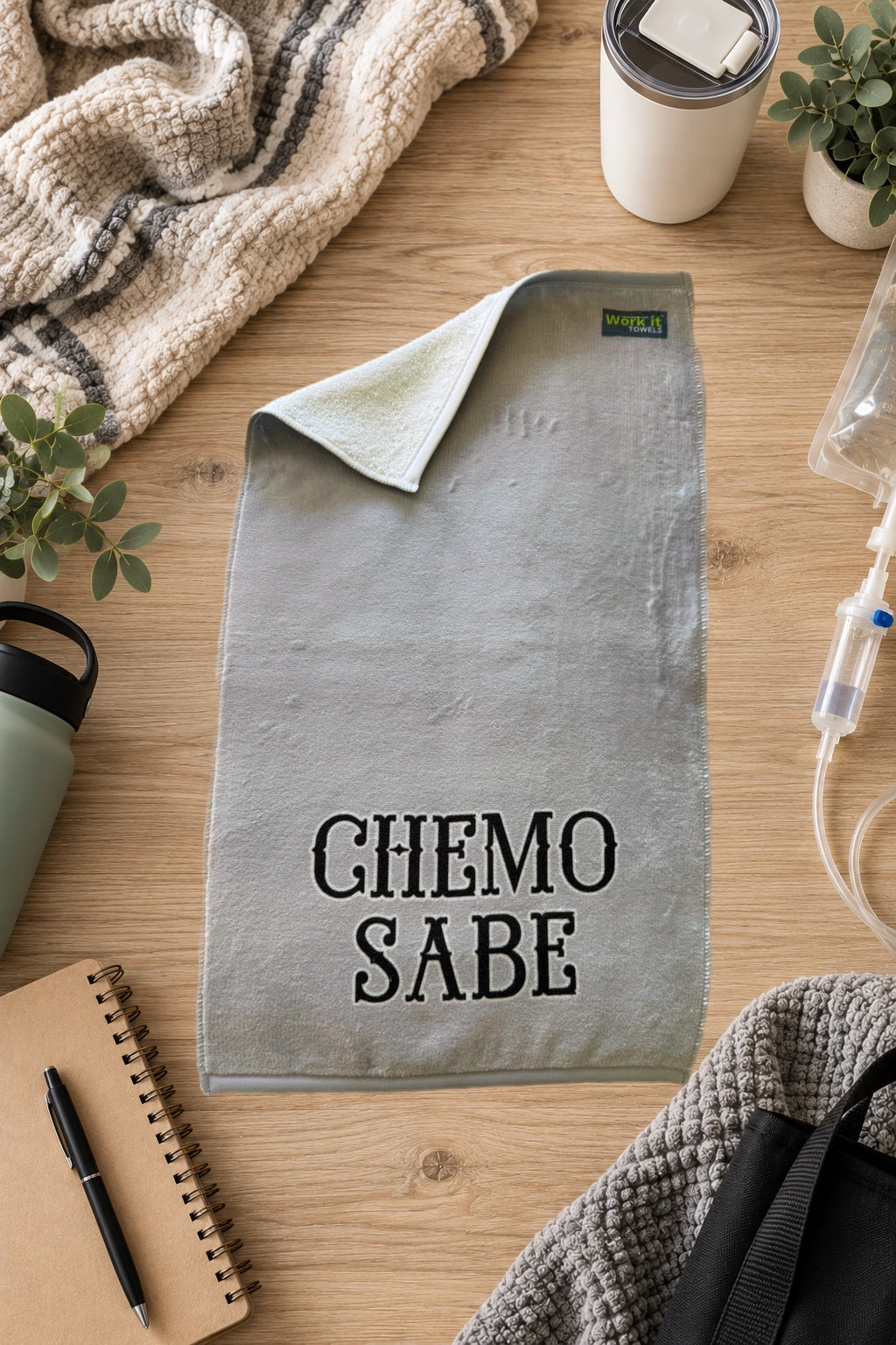 grey plush towel with 'chemo sabe' in black font on a hardwood floor with blankets and drinks