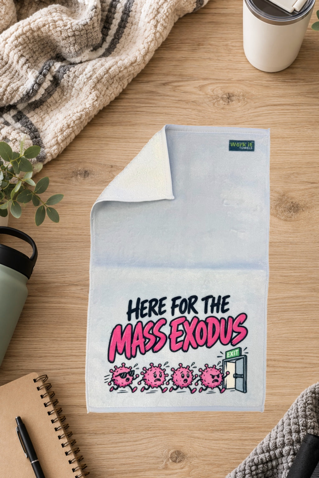 Light gray Here for the Mass Exodus towel with one corner folded back to show the soft white terry backing, on a wood table with a blanket and drinkware.
