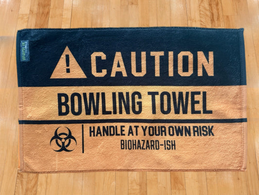 yellow and black caution towel with 'caution bowling towel, handle at your own risk, biohazardish' on shiny hardwood bowling floor
