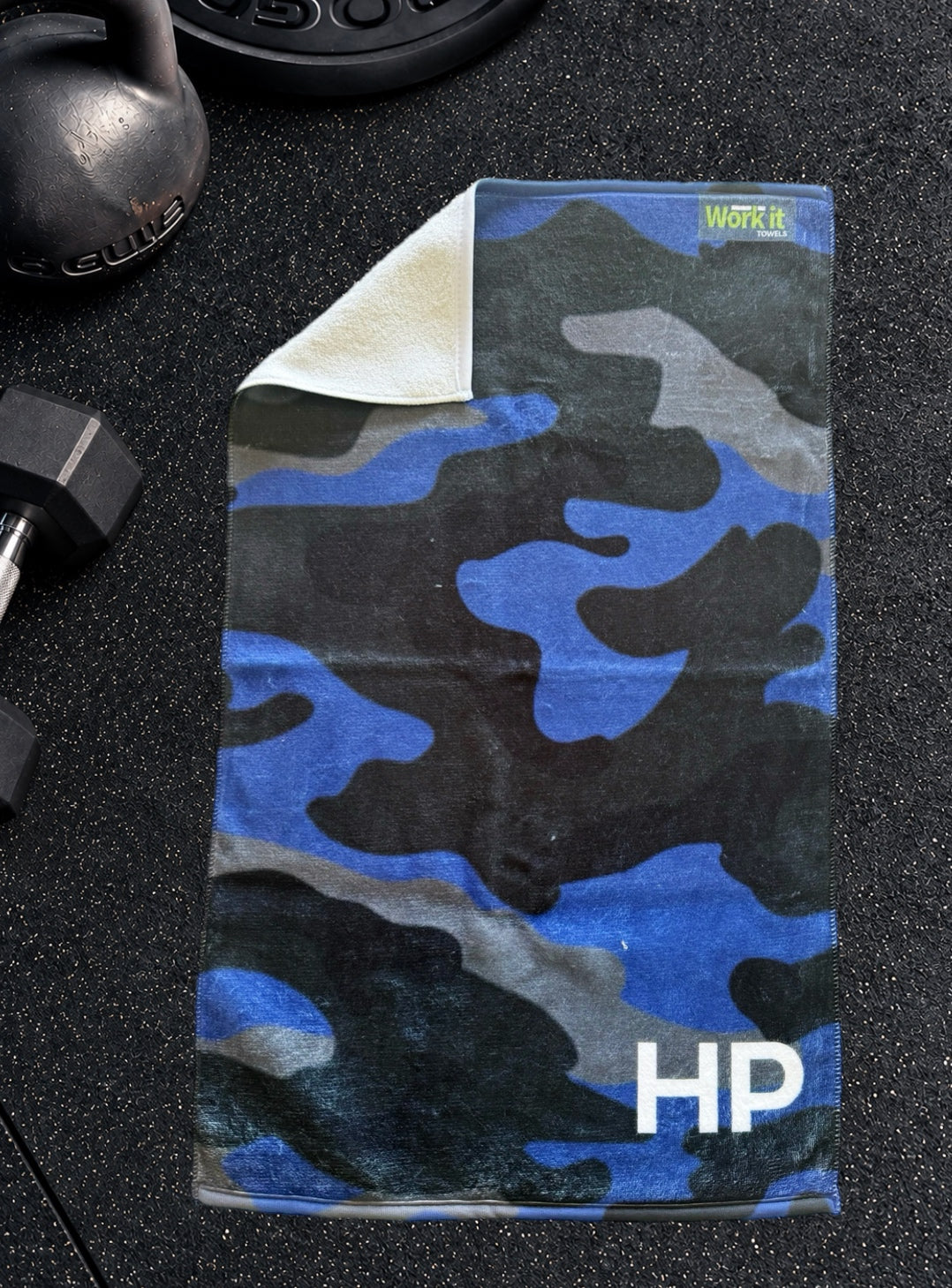Blue camouflage personalized gym towel with custom 'HP' initials, one corner folded back to show the soft white terry reverse side.