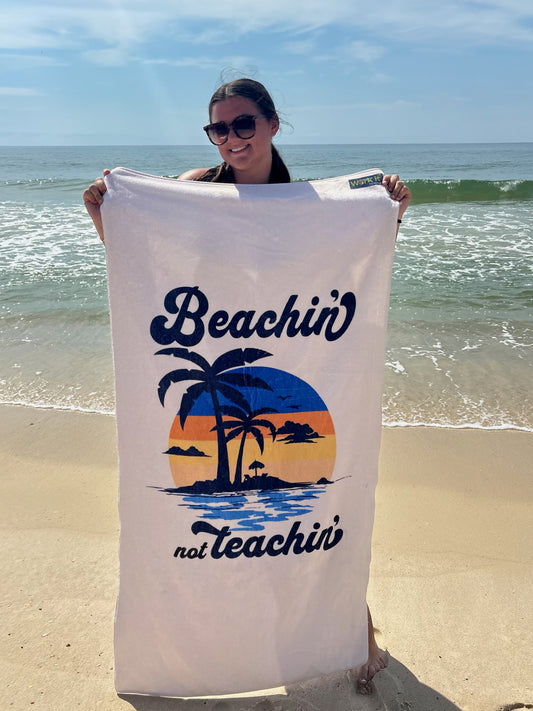 our 'beachin not teachin' sunset design beach towel being held by a young woman on a beach