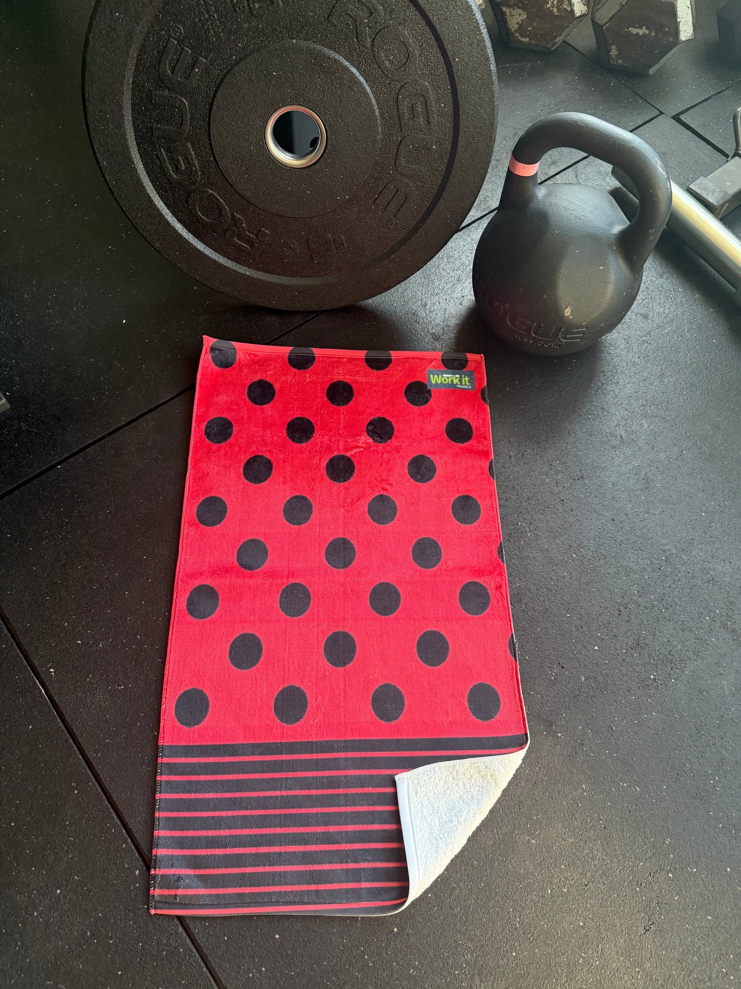 Red towel with black polka dots on a dark surface with gym equipment.