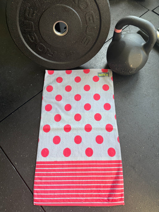 Polka dot towel with red circles and white stripes on a dark floor with gym equipment.