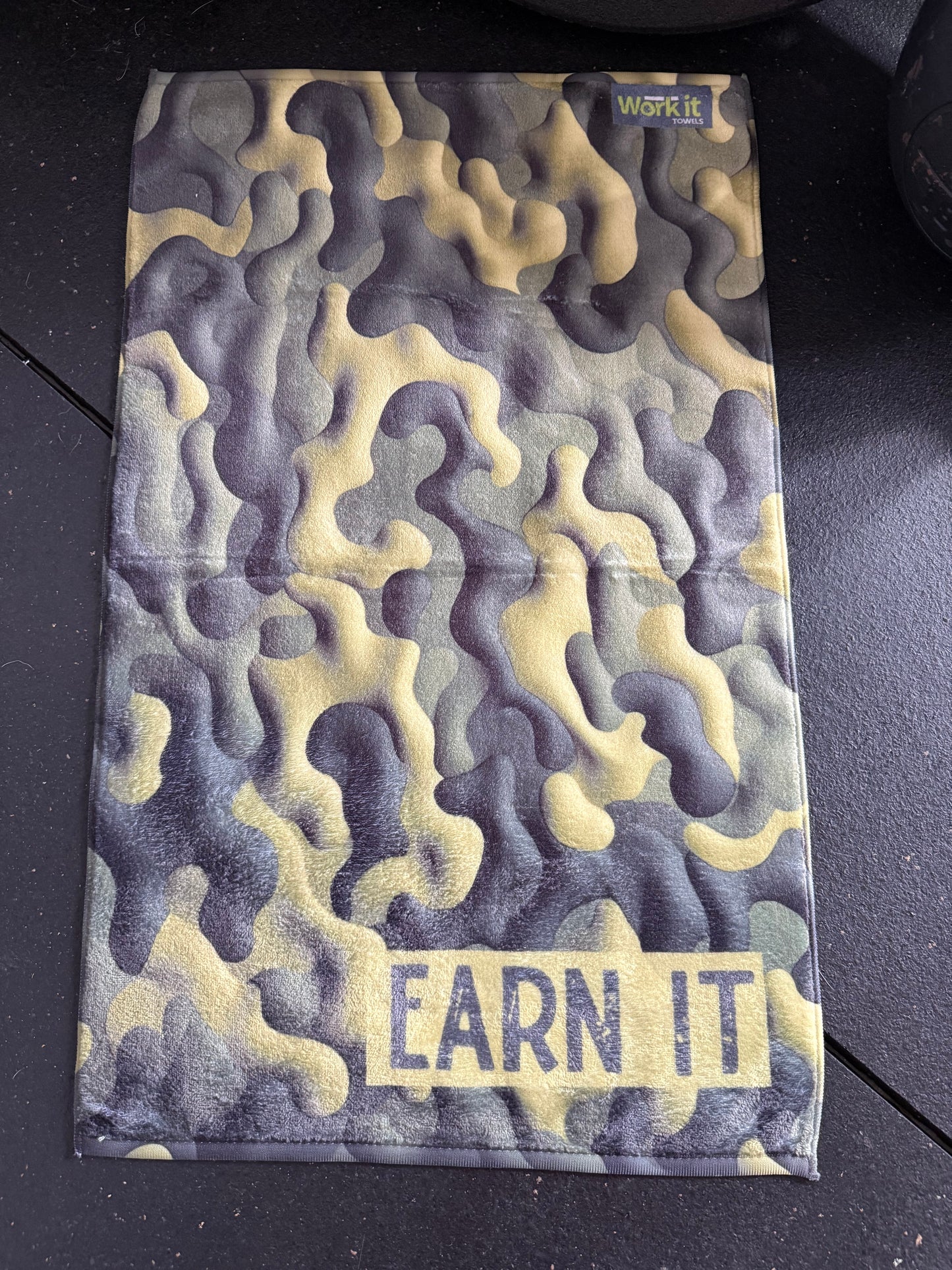 Camouflage-patterned pouch with 'EARN IT' text on a black surface