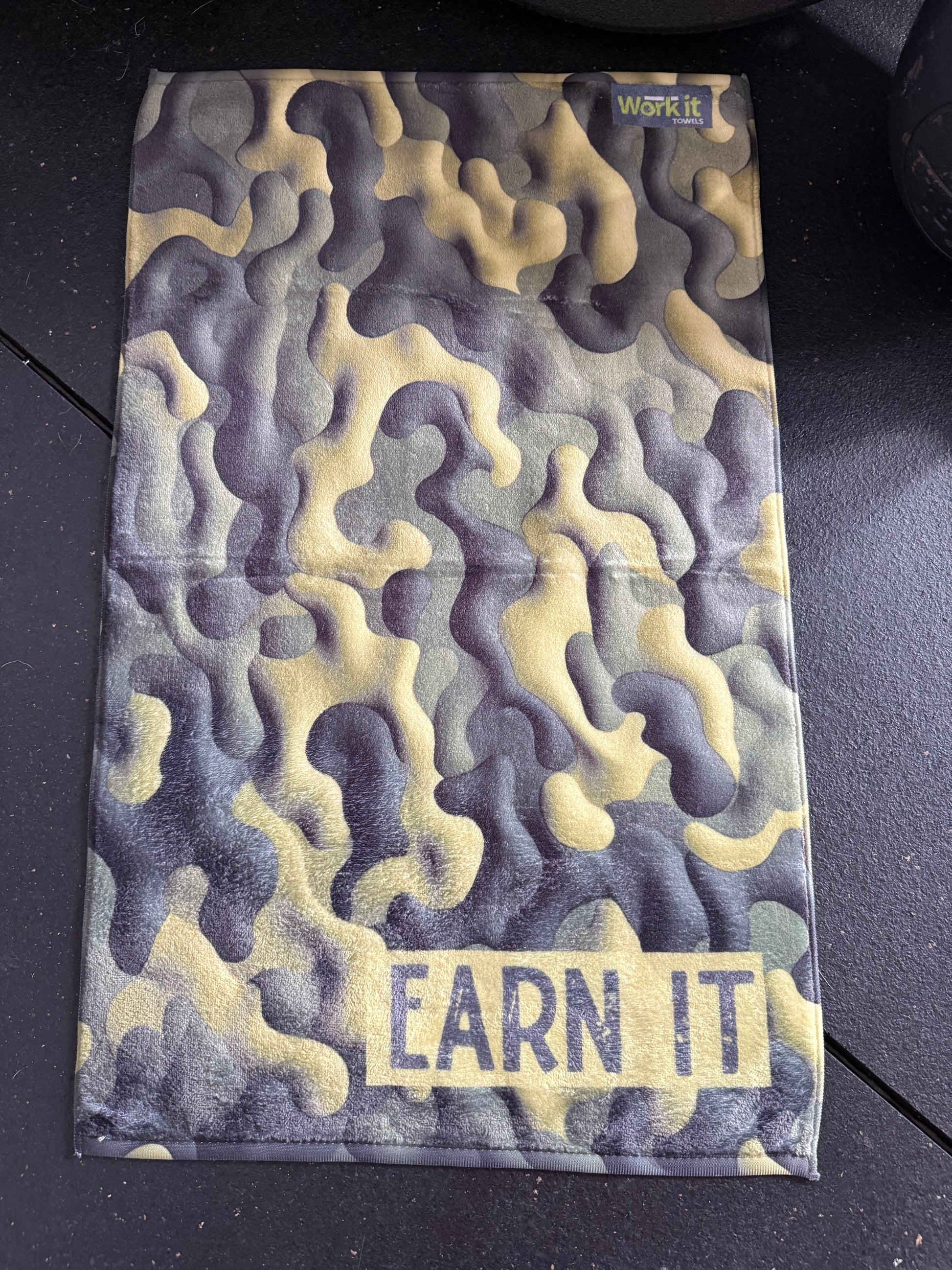 Camouflage-patterned pouch with 'EARN IT' text on a black surface