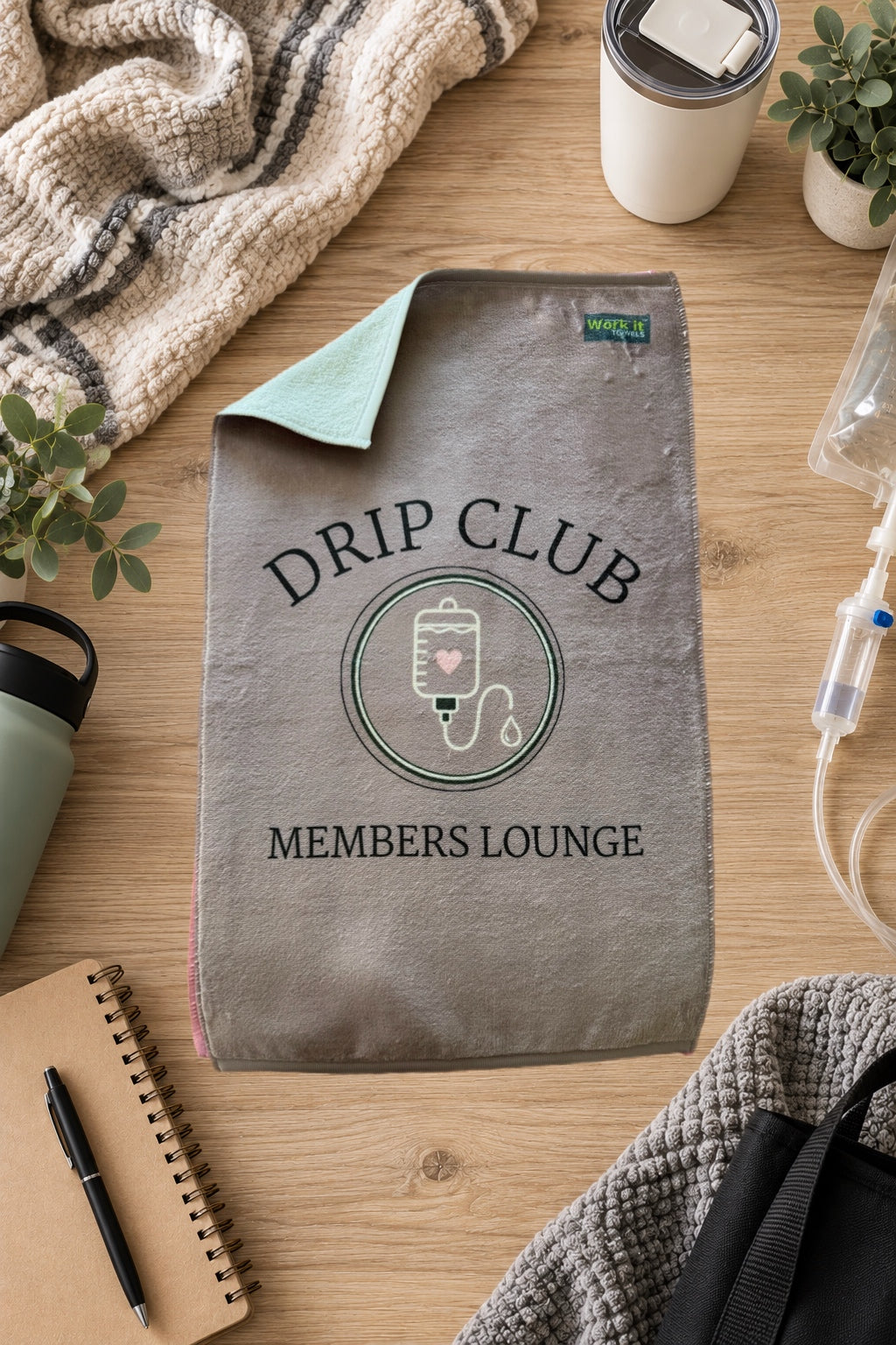 greyish mauve towel design with an IV and the font, 'drip club members lounge' on a hardwood floor with blankets and drinks 