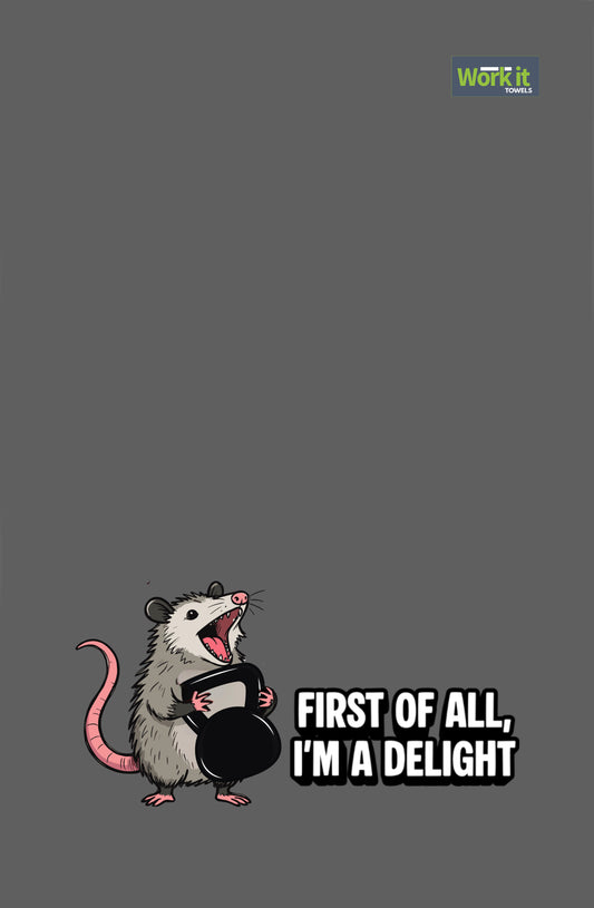 Dark gray towel with a cartoon opossum holding a kettlebell and the phrase “First of All, I’m a Delight.”