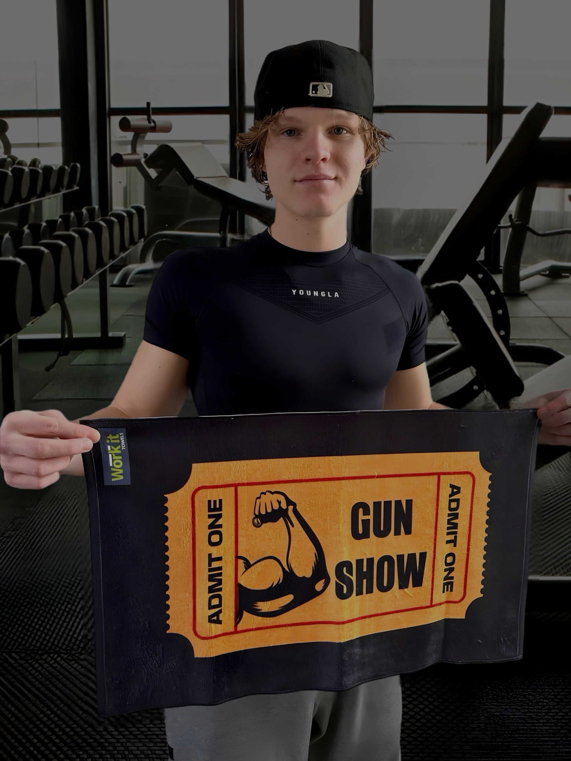 Fit male holding a sweat towel with 'ticket to the Gun Show' text and a flexing bicep image in a gym setting
