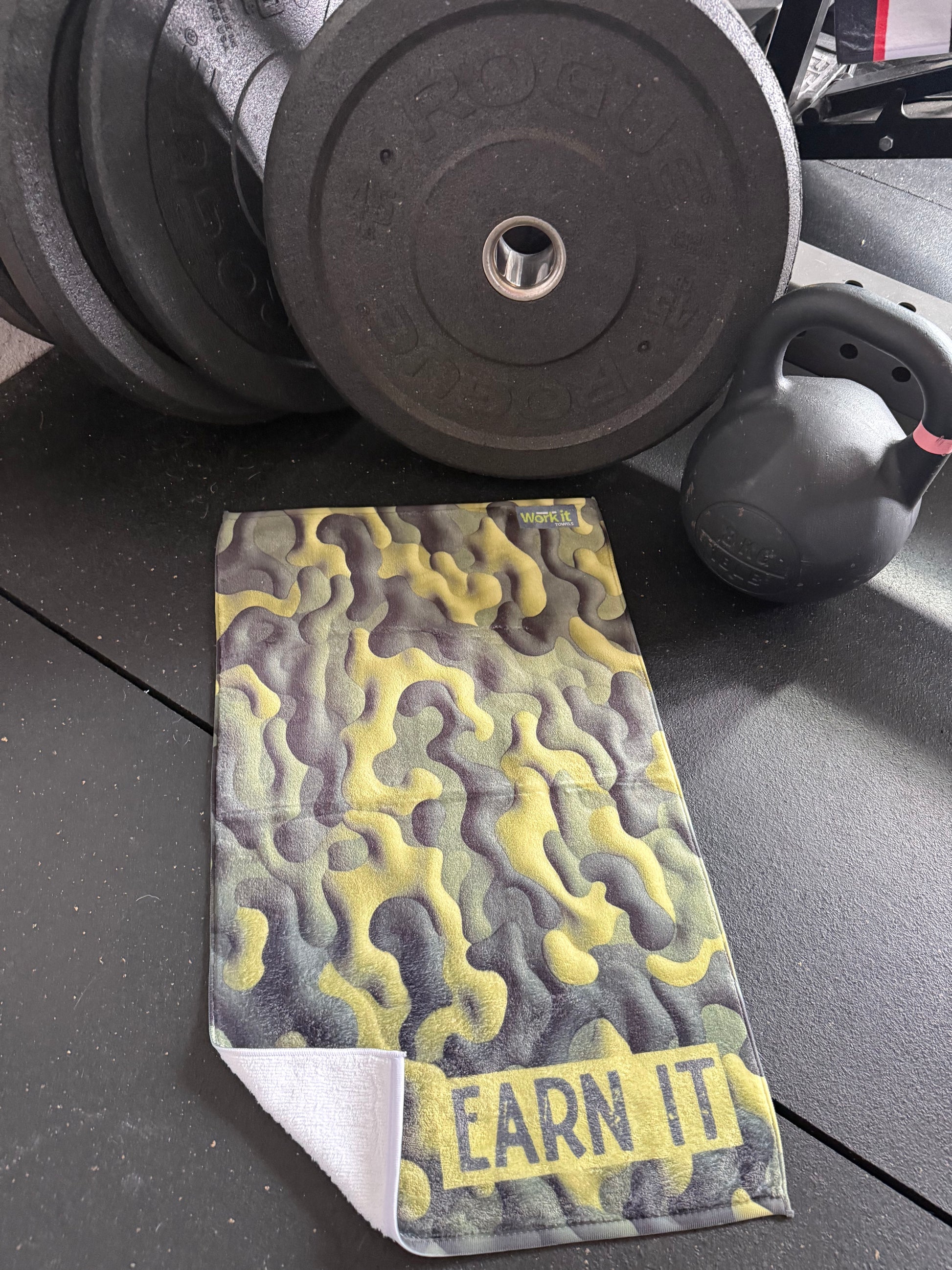 Stack of weight plates with a camouflage-patterned card labeled 'EARN IT' on a dark surface.