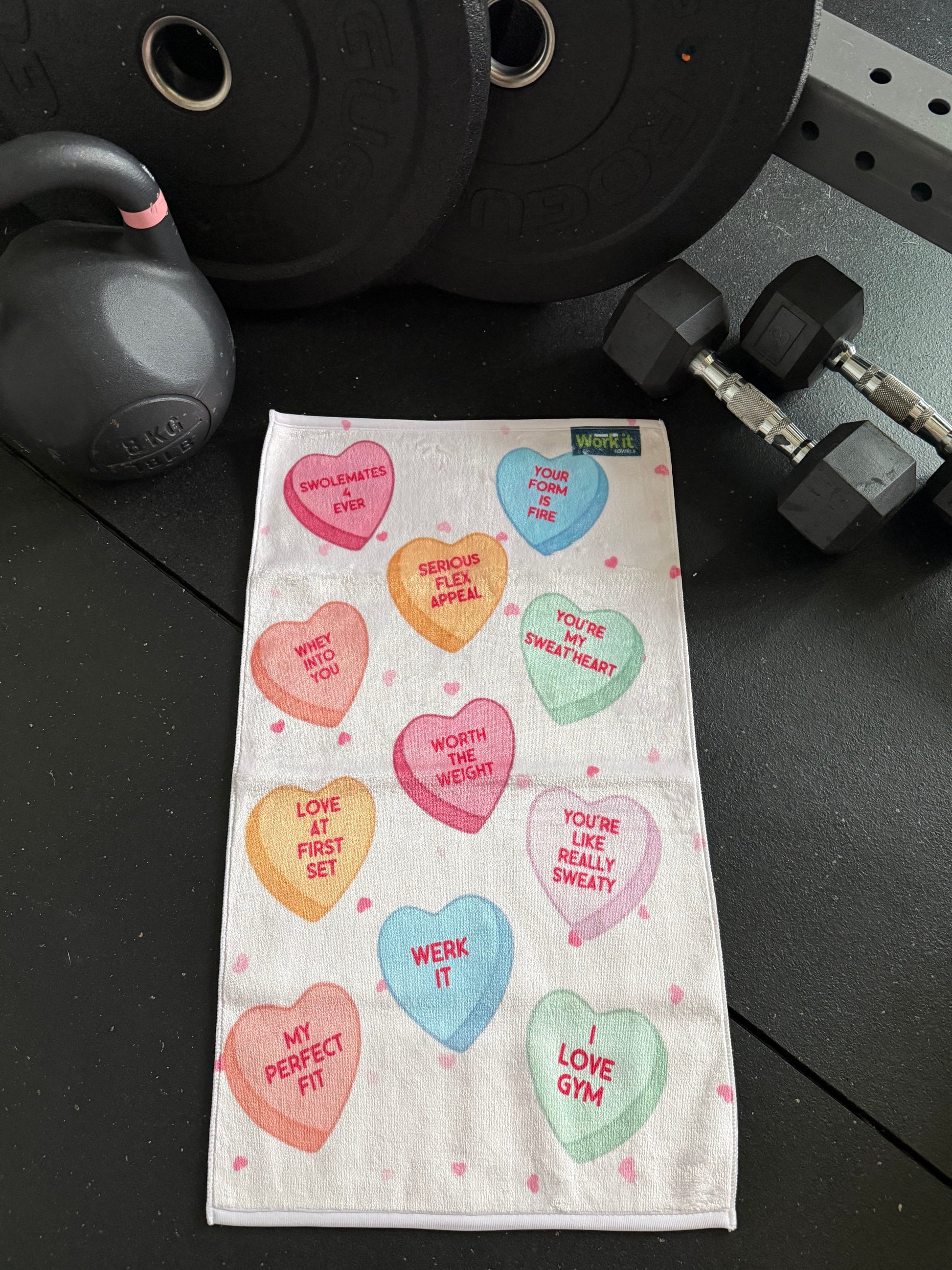 Gym towel with heart-shaped text on a black surface with gym equipment