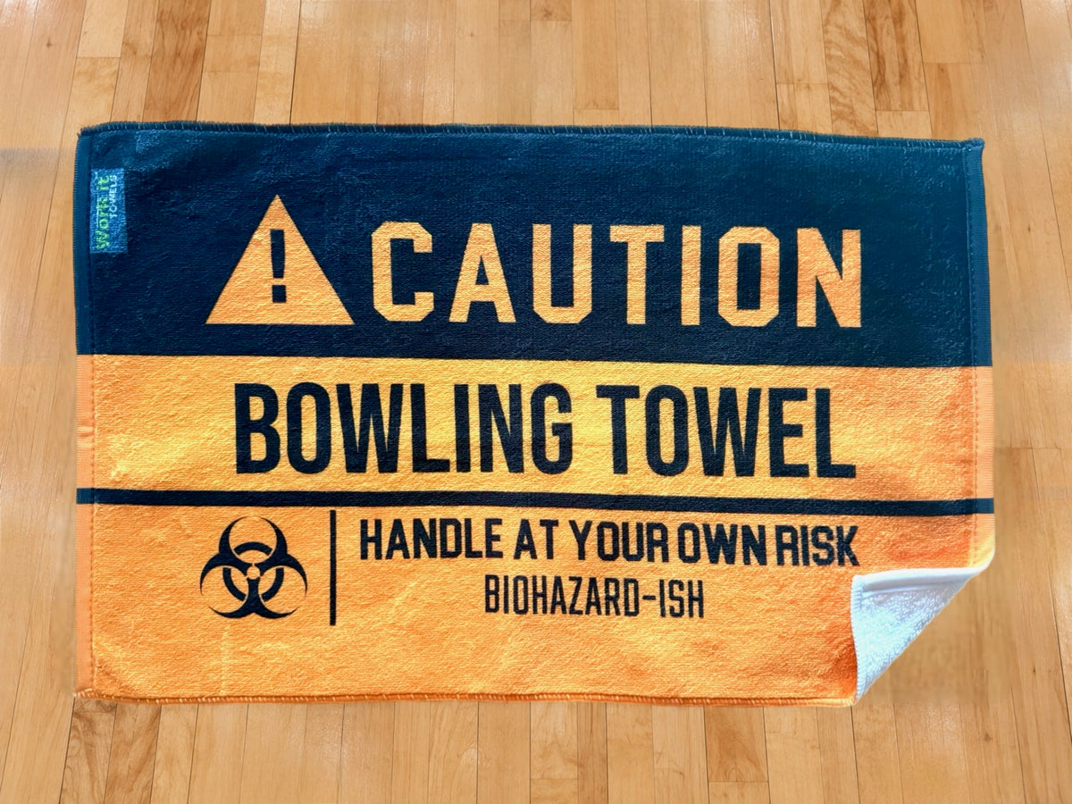 yellow and black caution towel  with 'caution bowling towel, handle at your own risk, biohazardish' on shiny hardwood bowling floor