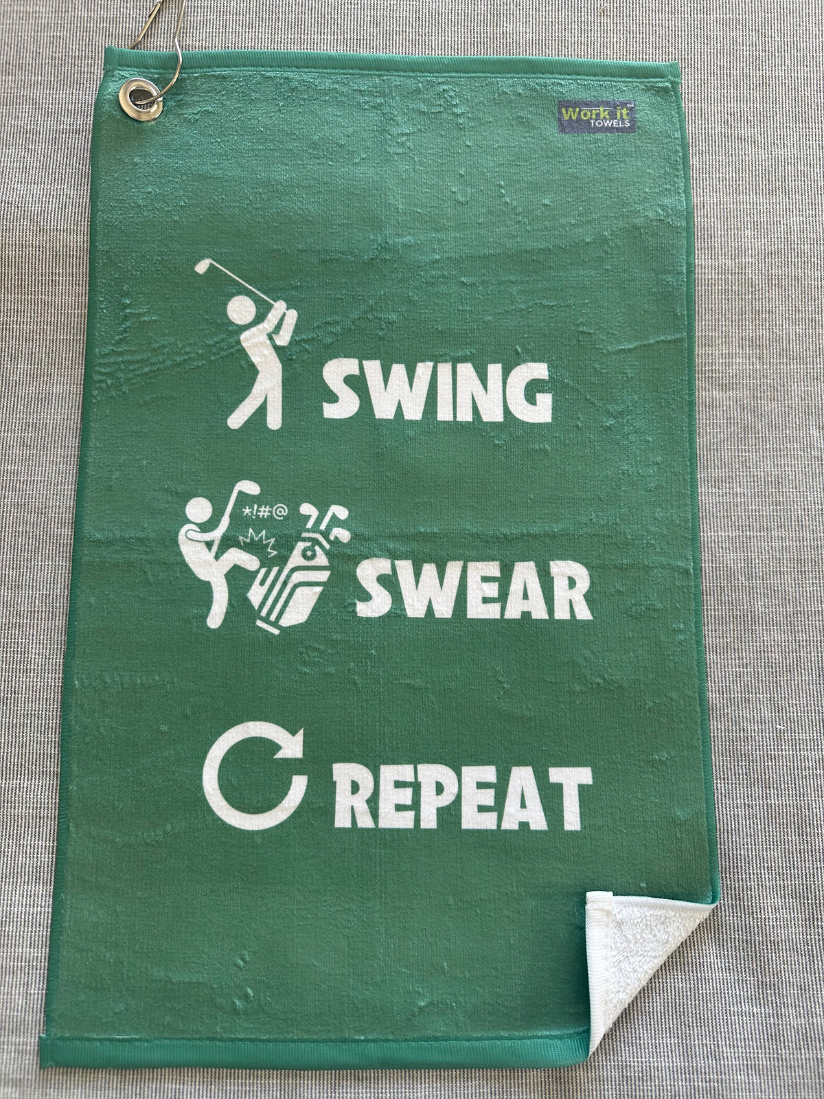 green golf towel with 'swing swear repeat' text and coordinating graphics (golf swinger, kicking clubs, arrow) in white font.  Includes hook and grommet. 