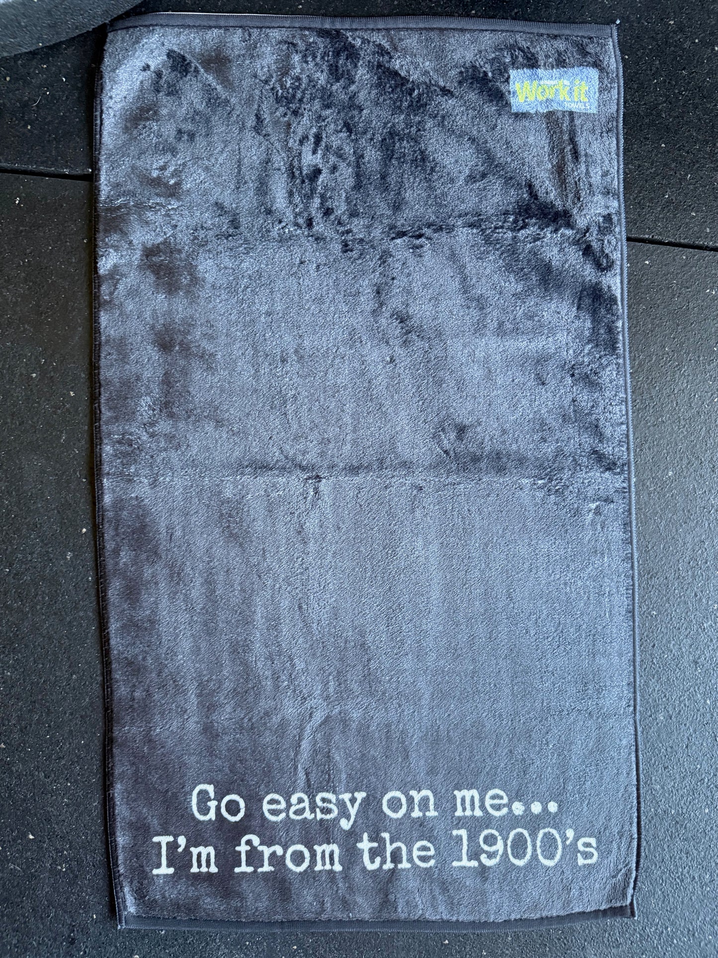 Black gym towel with 'Go easy on me... I'm from the 1900's' text on a textured surface.
