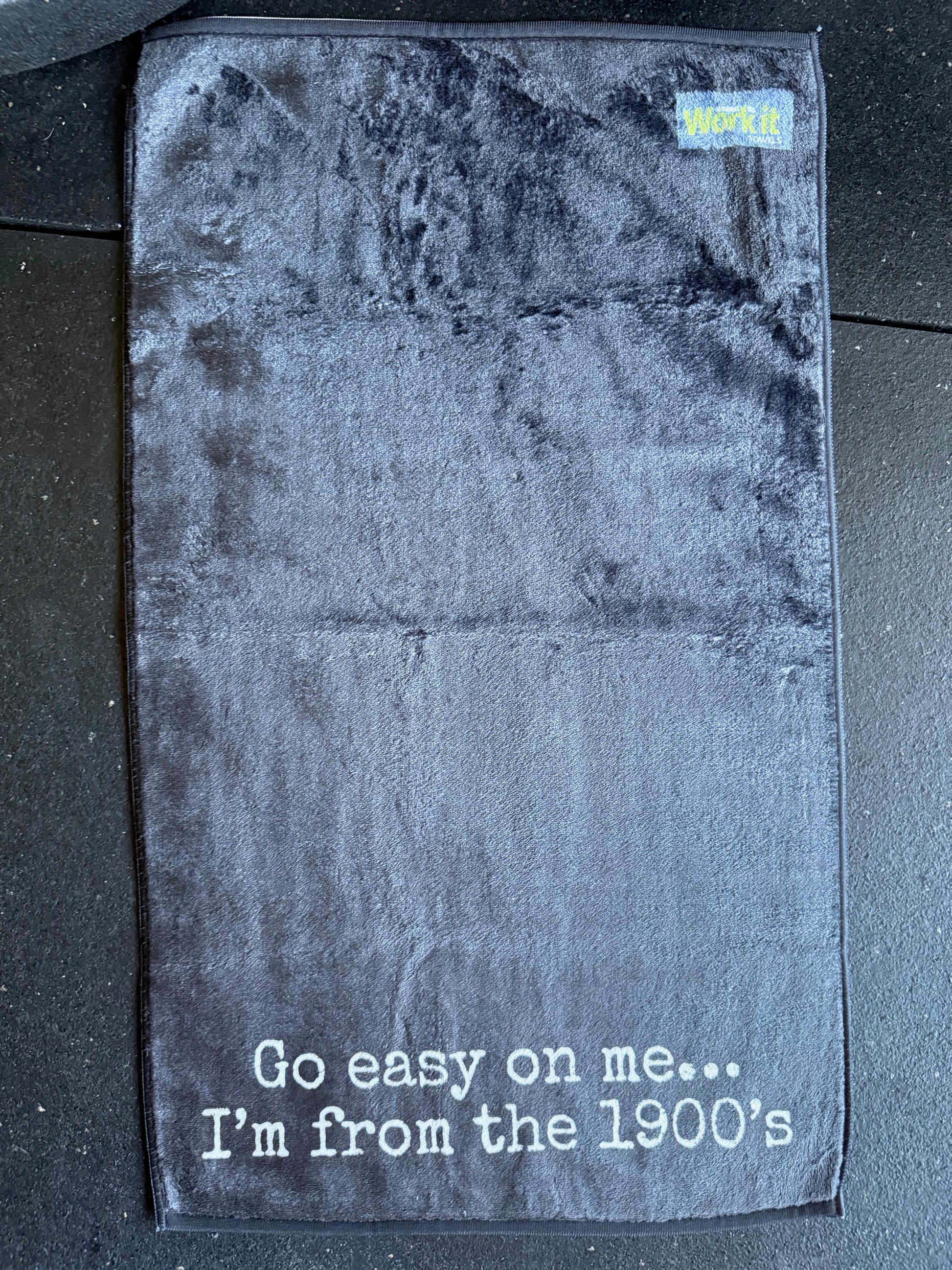 Black gym towel with 'Go easy on me... I'm from the 1900's' text on a textured surface.