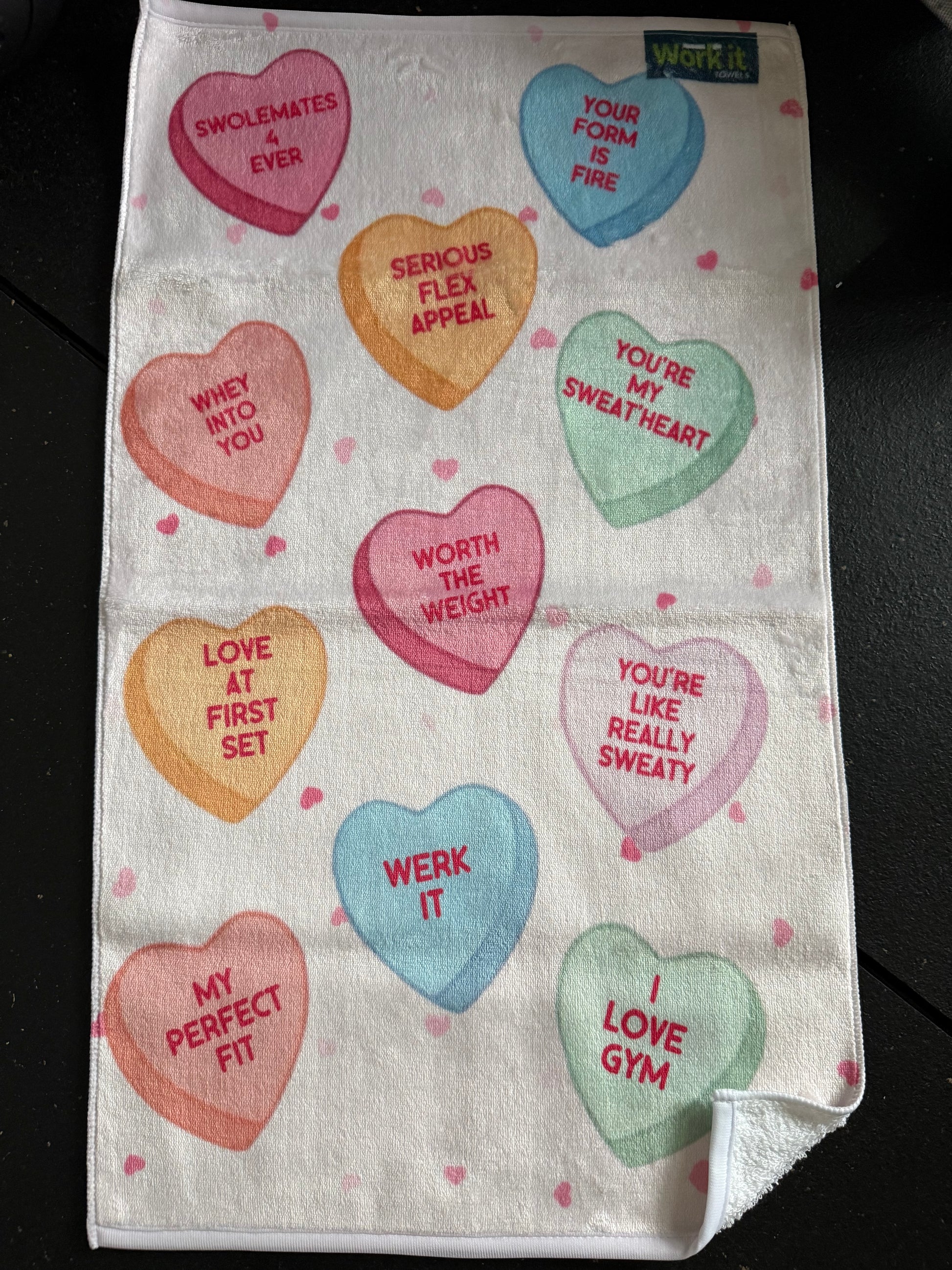 Towel with colorful conversation heart-shaped sayings on a black surface
