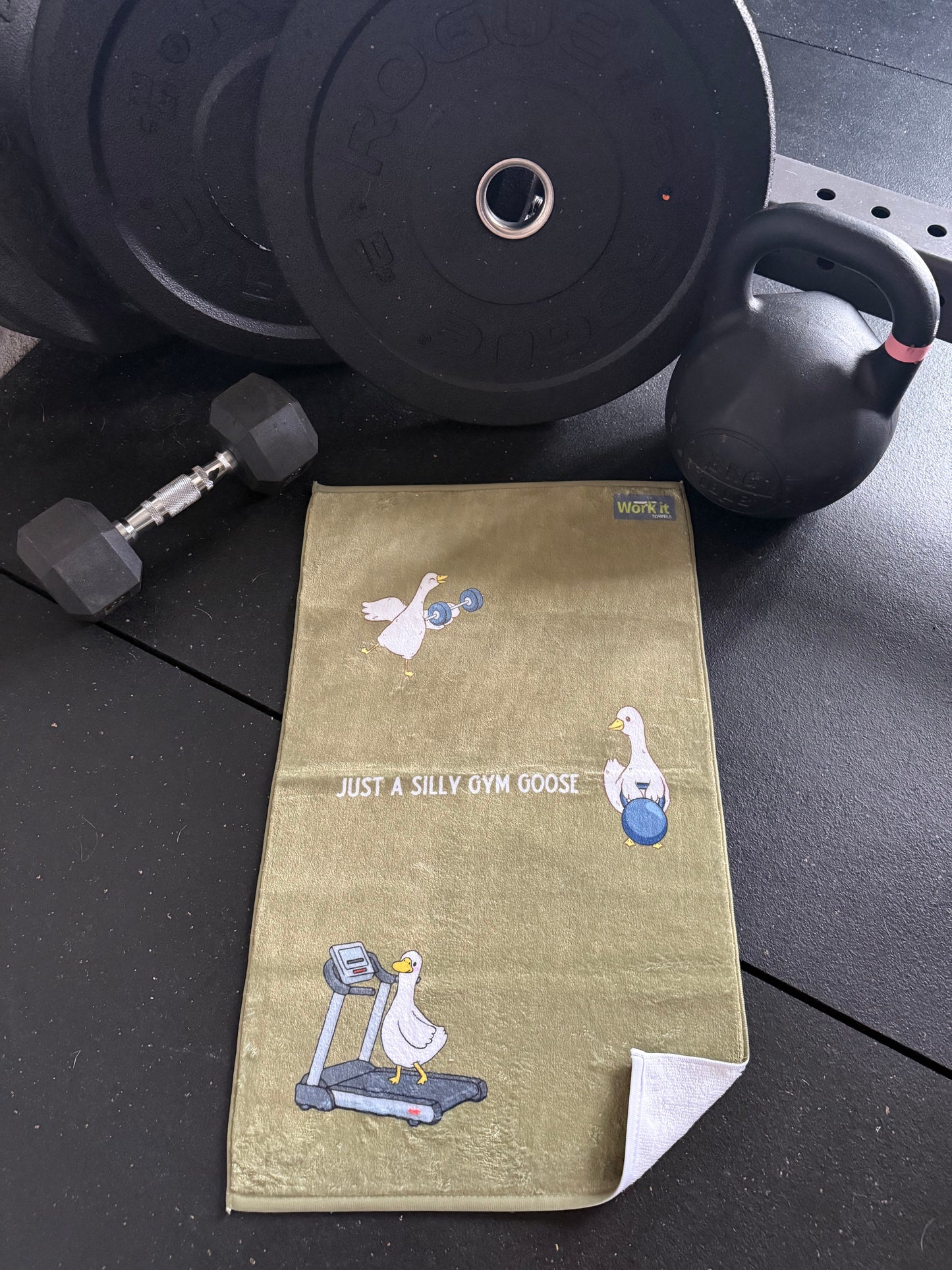 Gym towel with cartoon silly goose designs on a gym floor with weights and dumbbells.