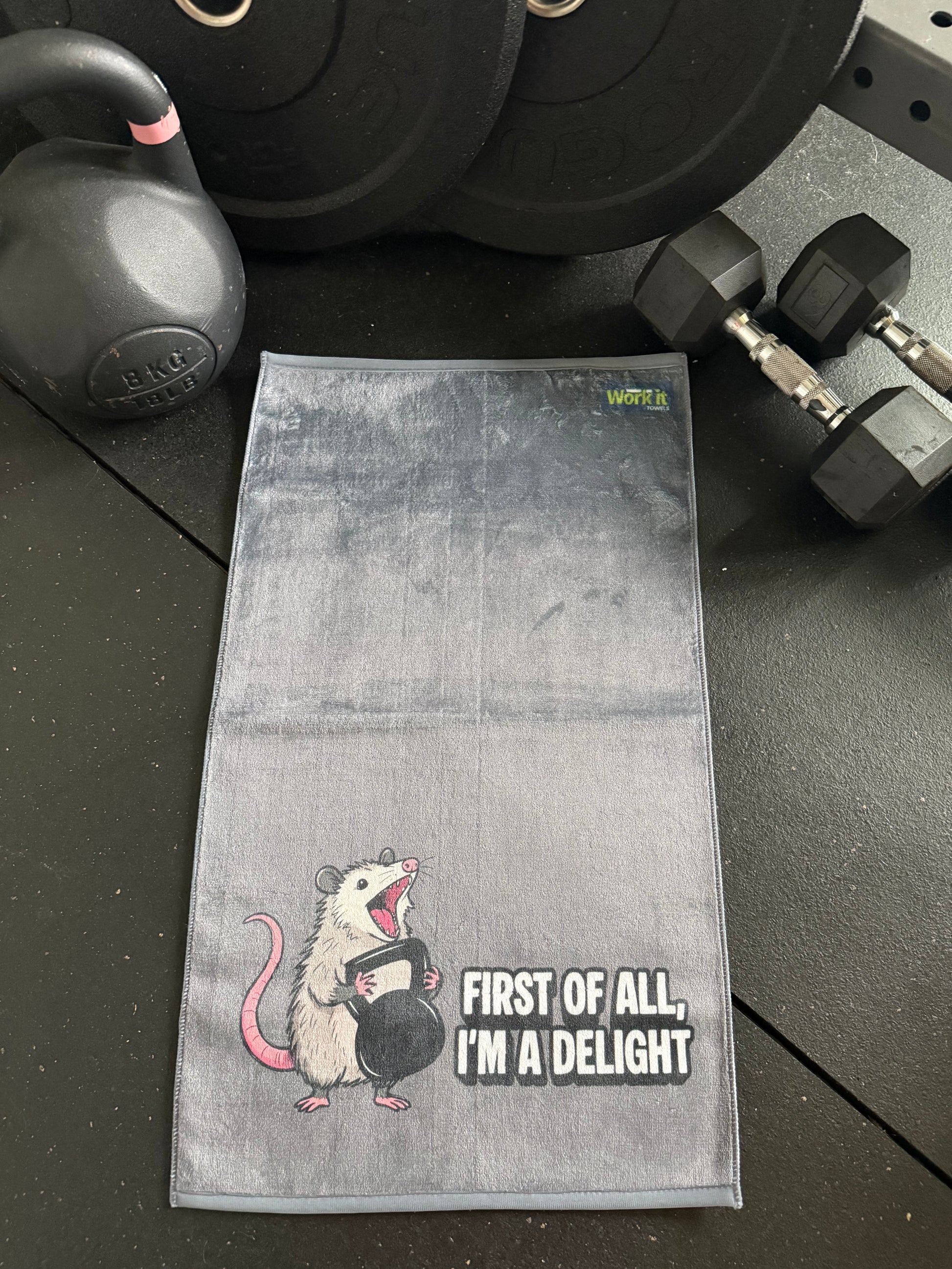Gray towel with a cartoon mouse design and text on a black surface with weights.