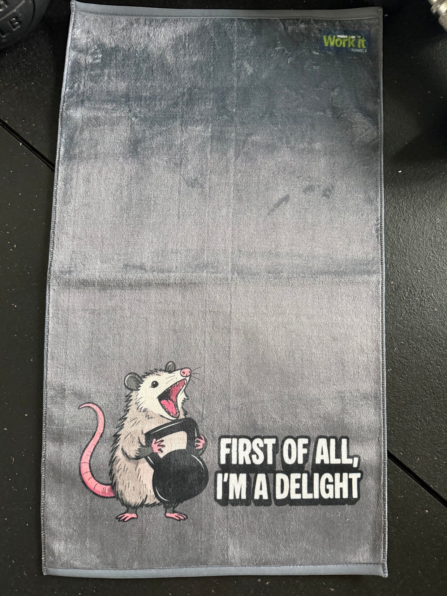 Gray towel with a cartoon opossum and text on a dark surface