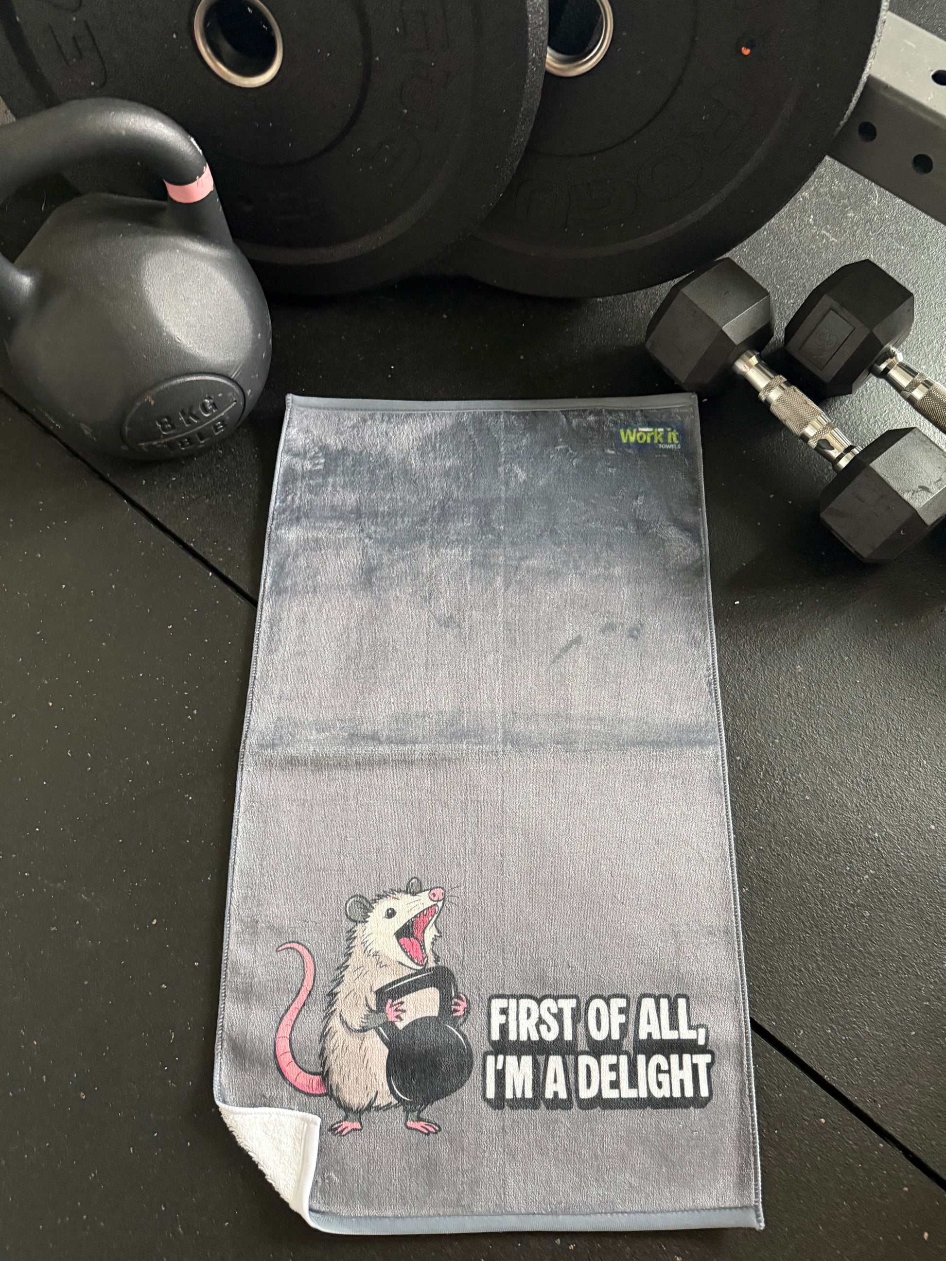 Gray towel with cartoon mouse design and text on a black surface with gym equipment.