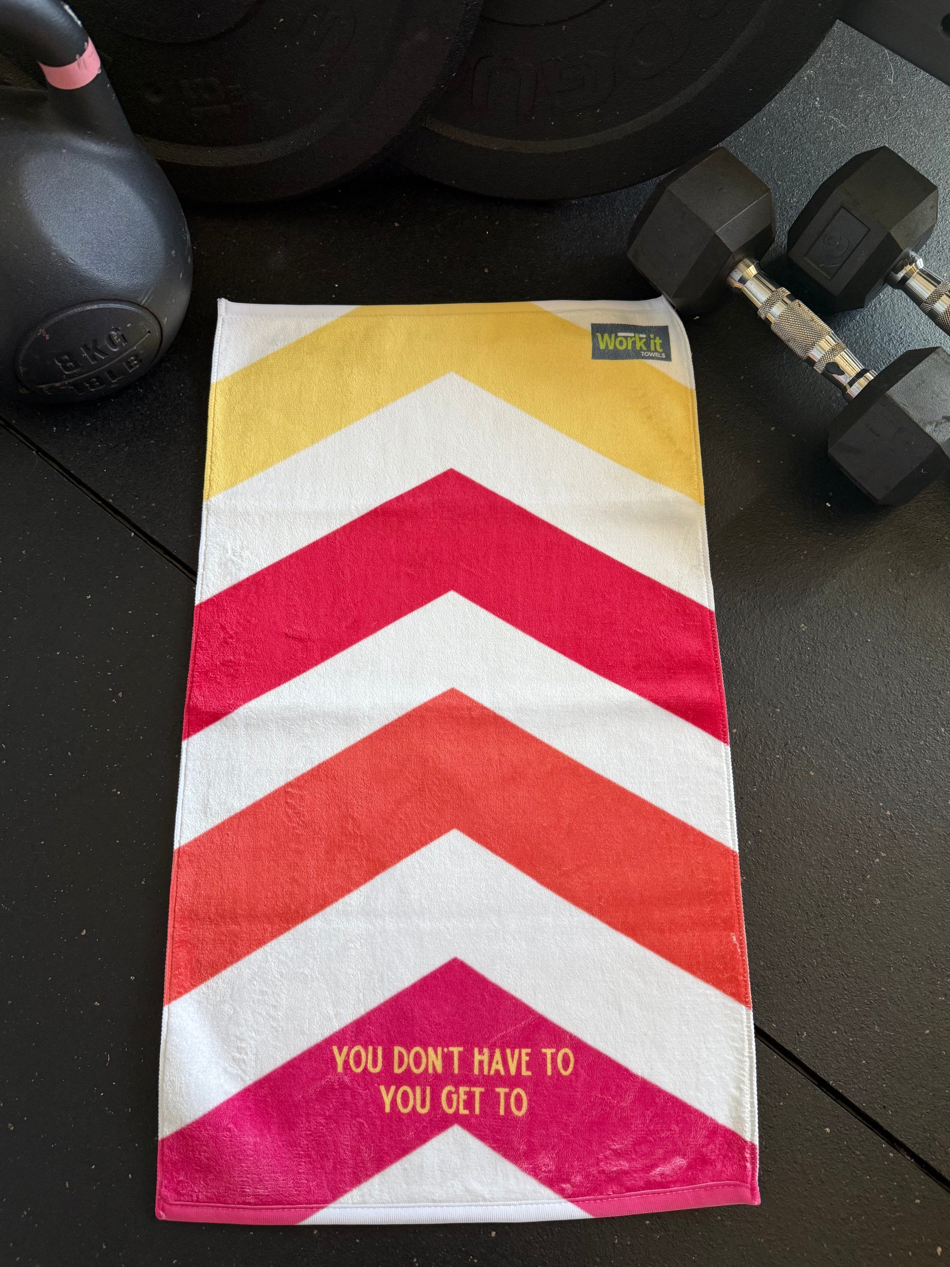 Striped towel with motivational quote on a black surface with dumbbells