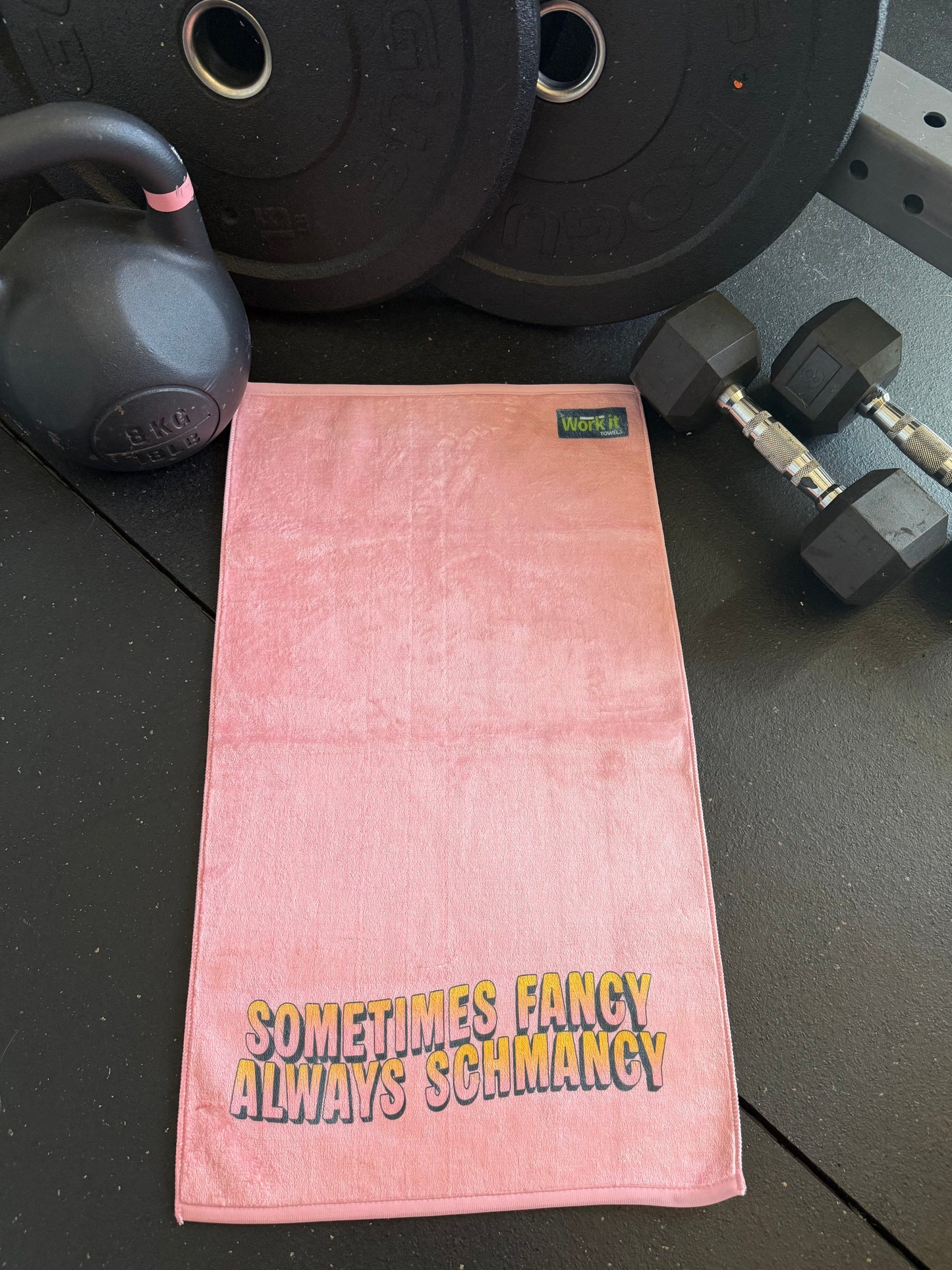 Pink towel with text on a black surface with gym equipment