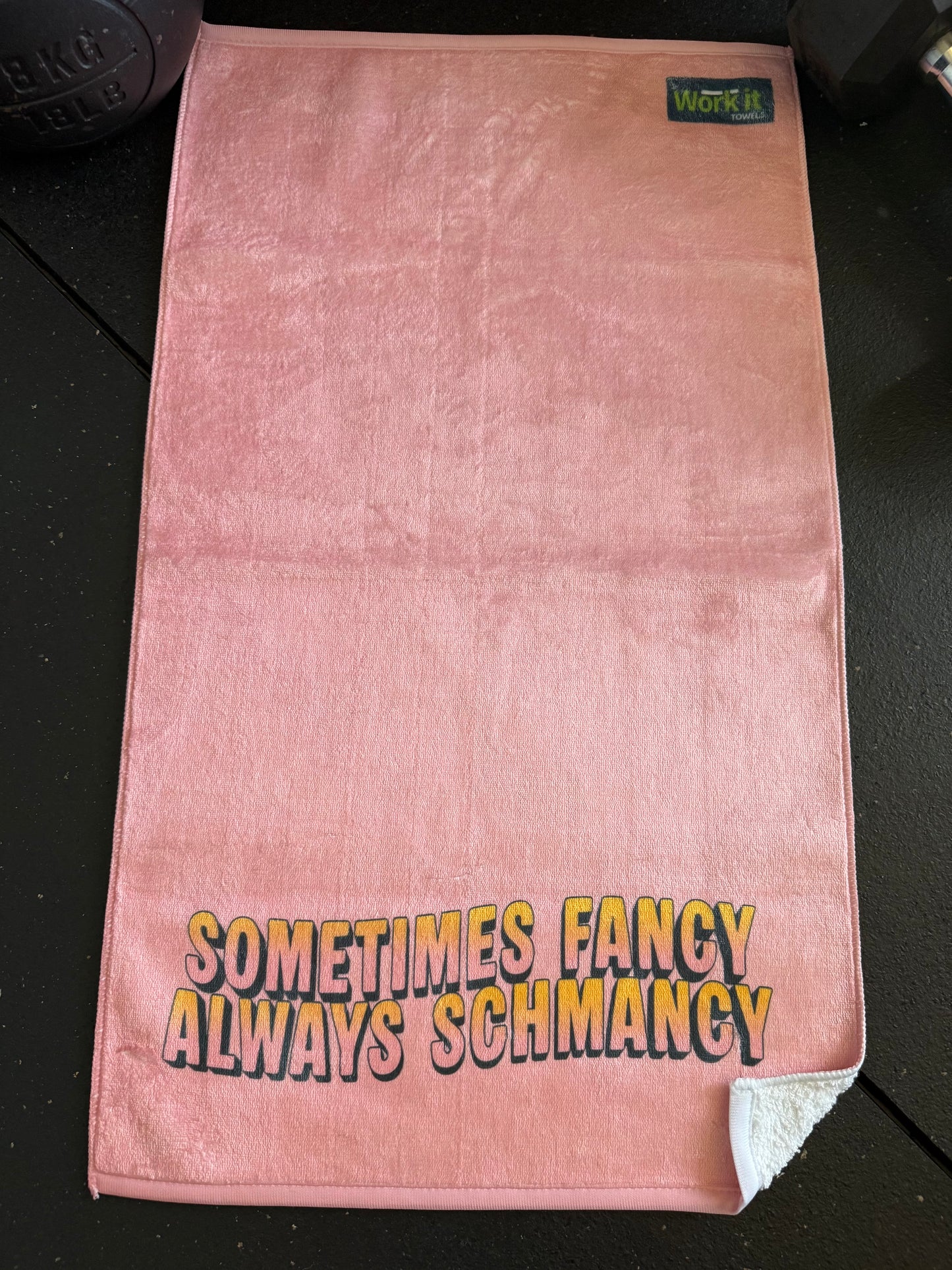 Pink towel with text 'Sometimes Fancy Always Schmancy' on a black surface