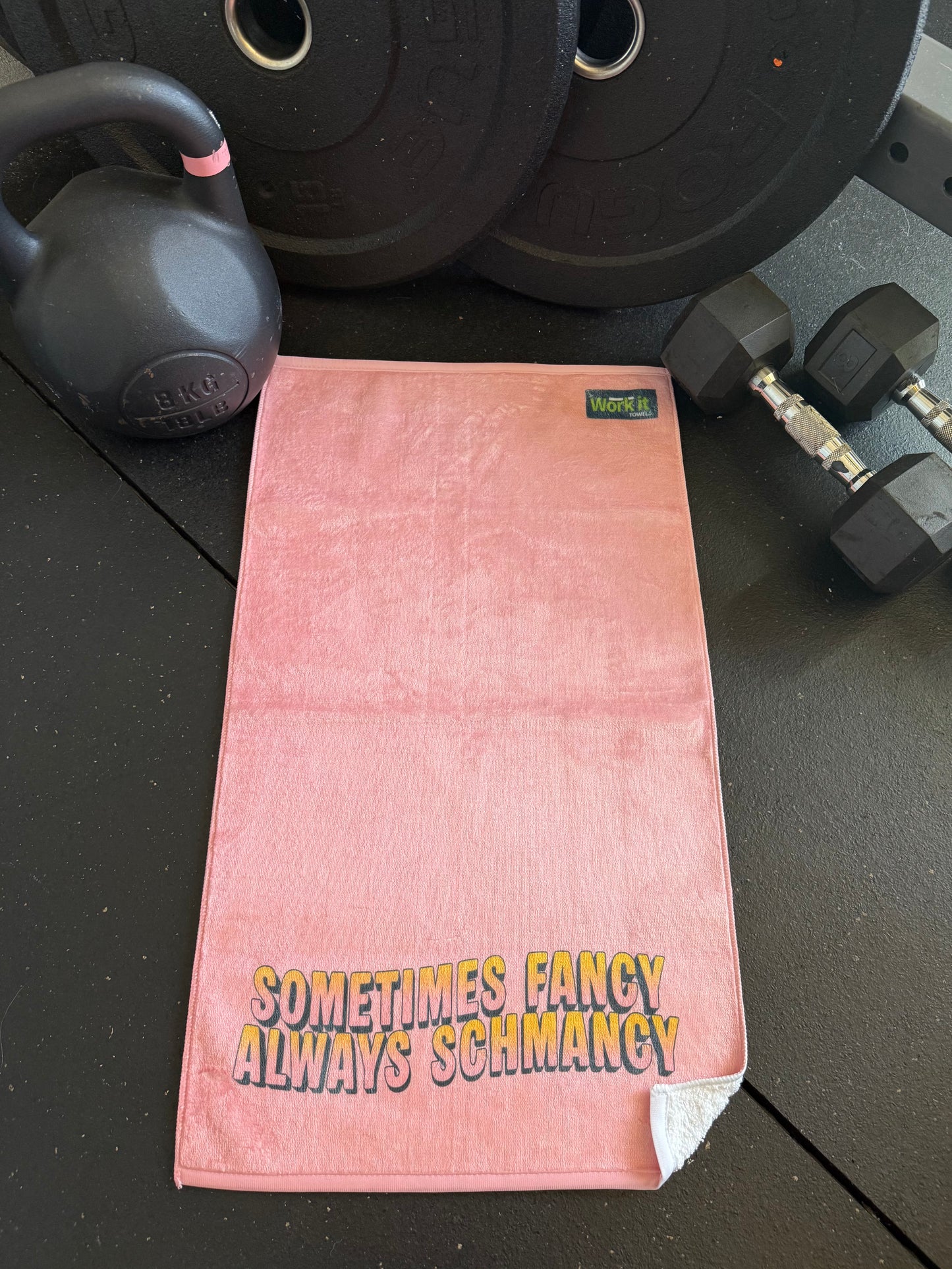 Pink towel with text on a gym floor with weights in the background