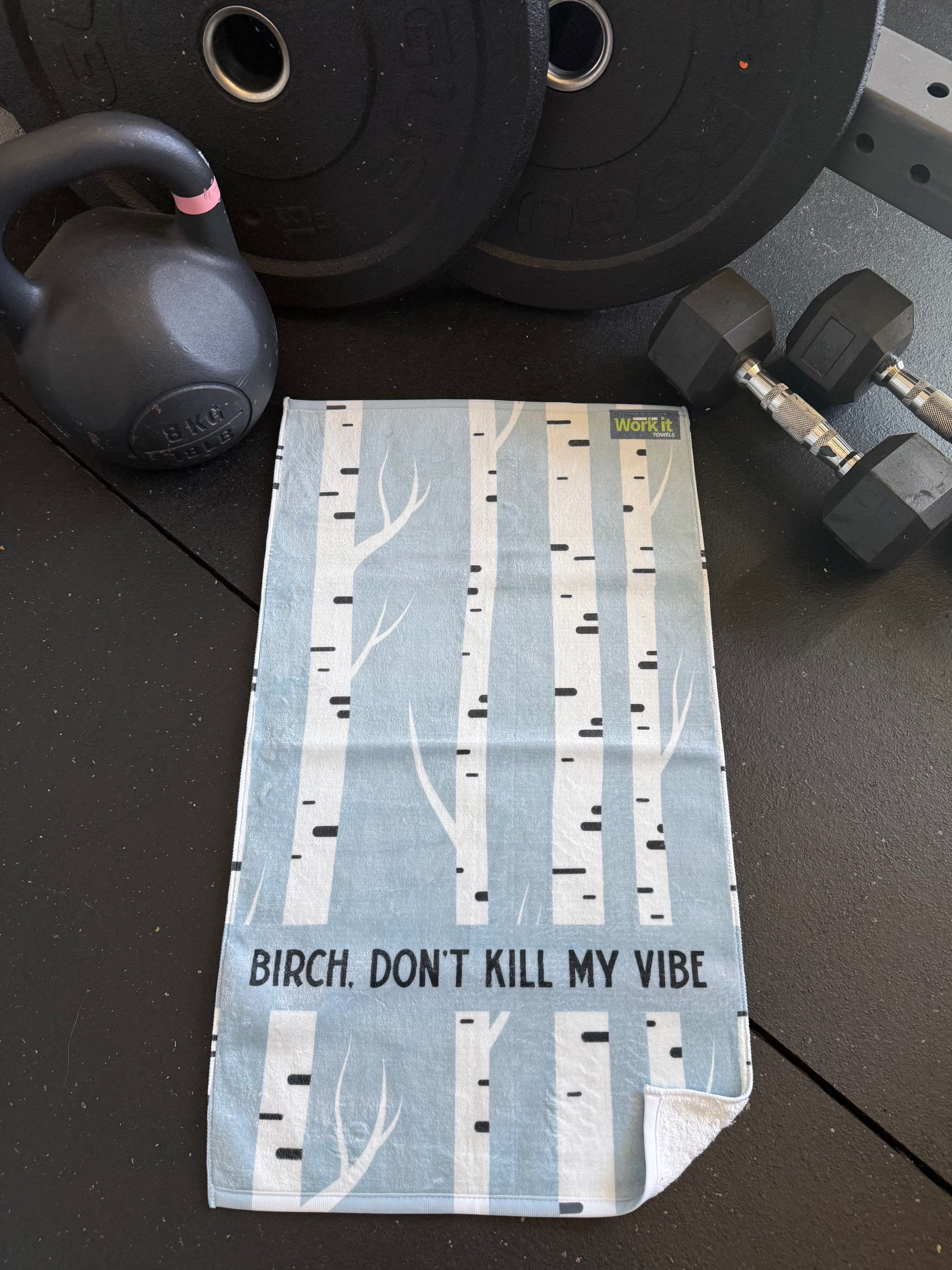 Fitness towel with birch tree design and text that says,' birch don't kill my vibe' on a gym floor with weights and kettlebell.