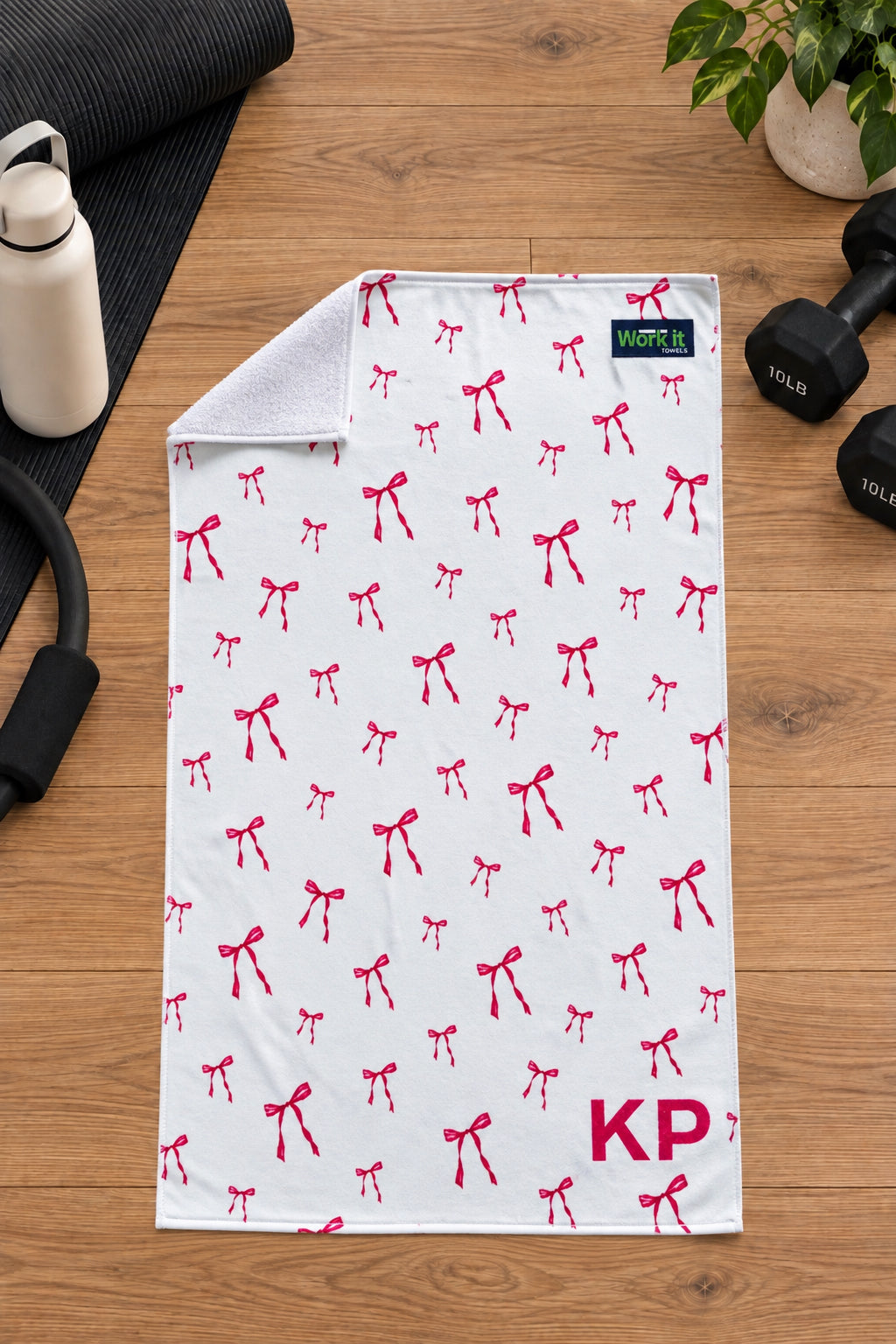 Pink bow personalized gym towel with custom 'KP' initials, one corner folded back to show the soft white terry reverse side.