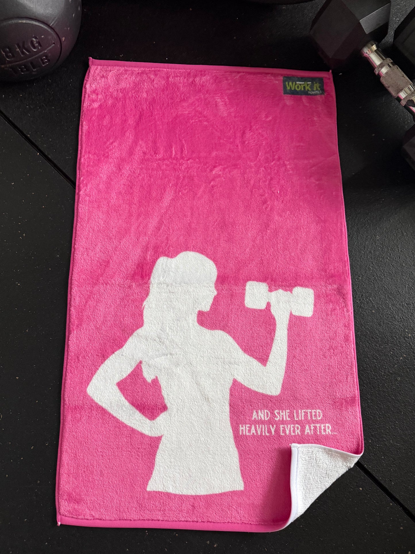 Pink towel with white silhouette of a woman lifting weights and text on a black surface