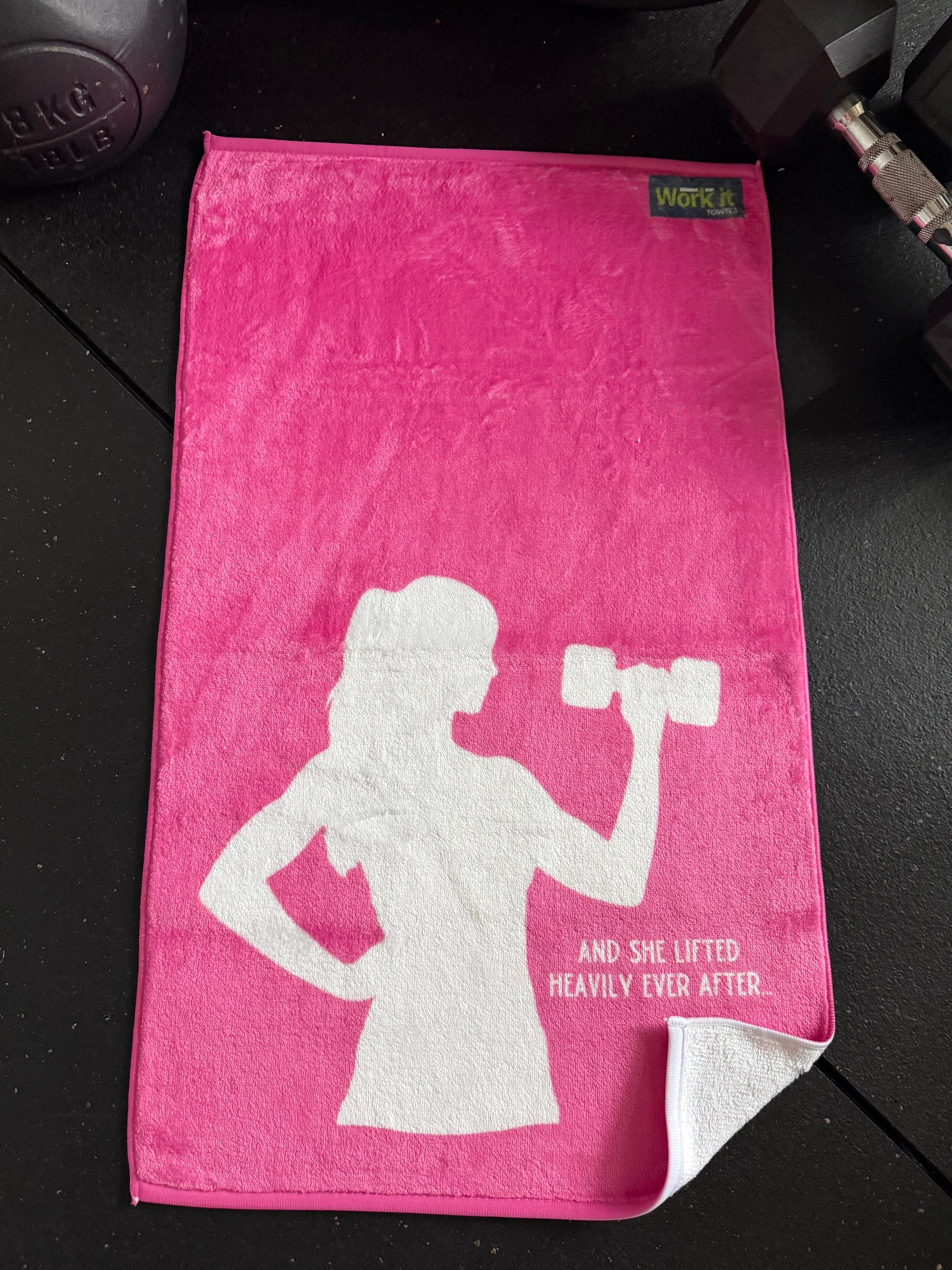 Pink towel with white silhouette of a woman lifting weights and text on a black surface