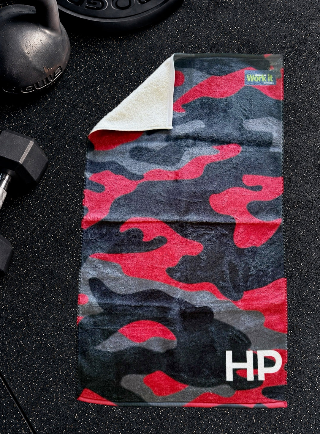 Red camouflage personalized gym towel with custom 'HP' initials, one corner folded back to show the soft white terry reverse side.