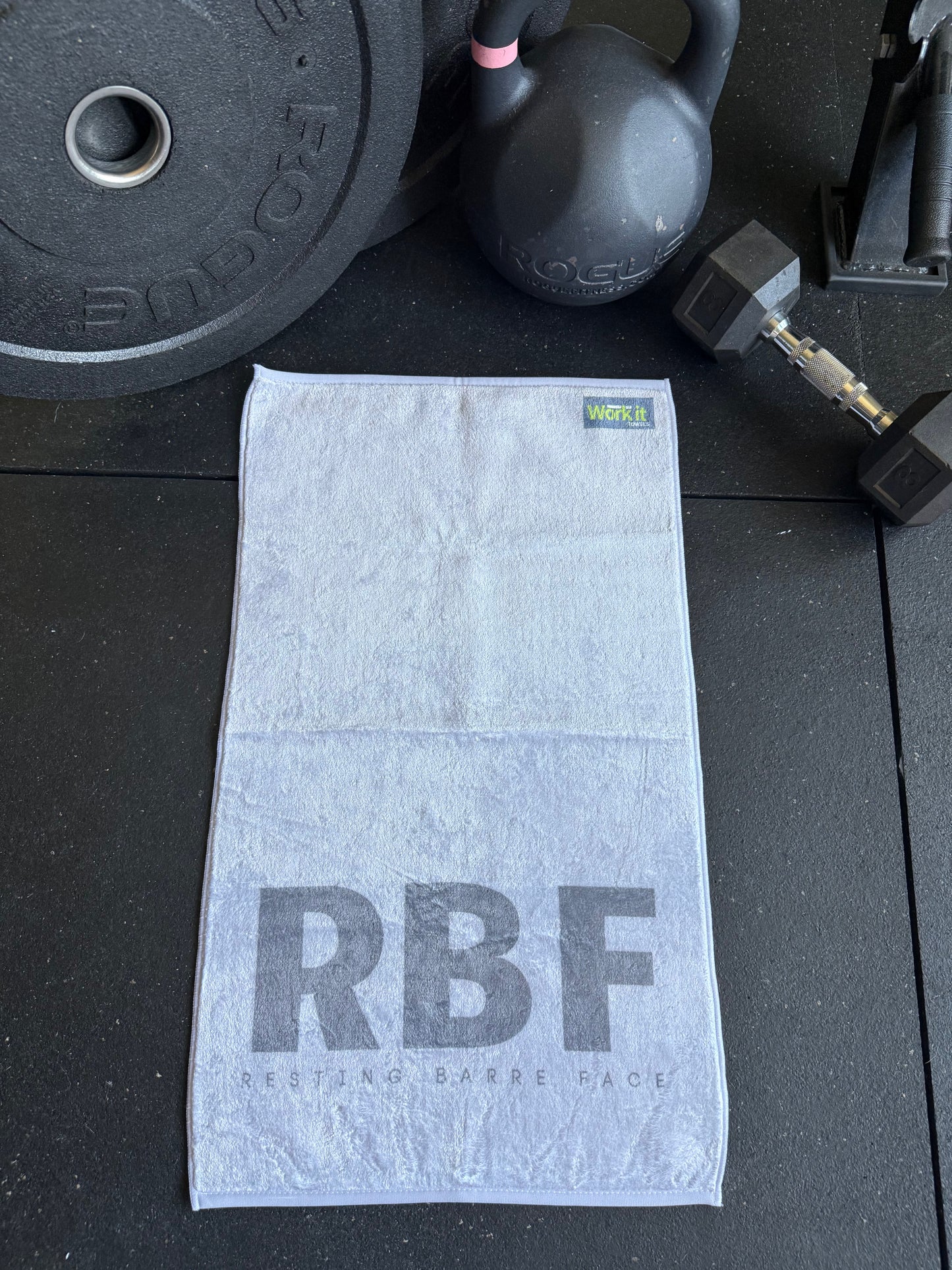 Gray towel with 'RBF' branding on a black surface with fitness equipment.
