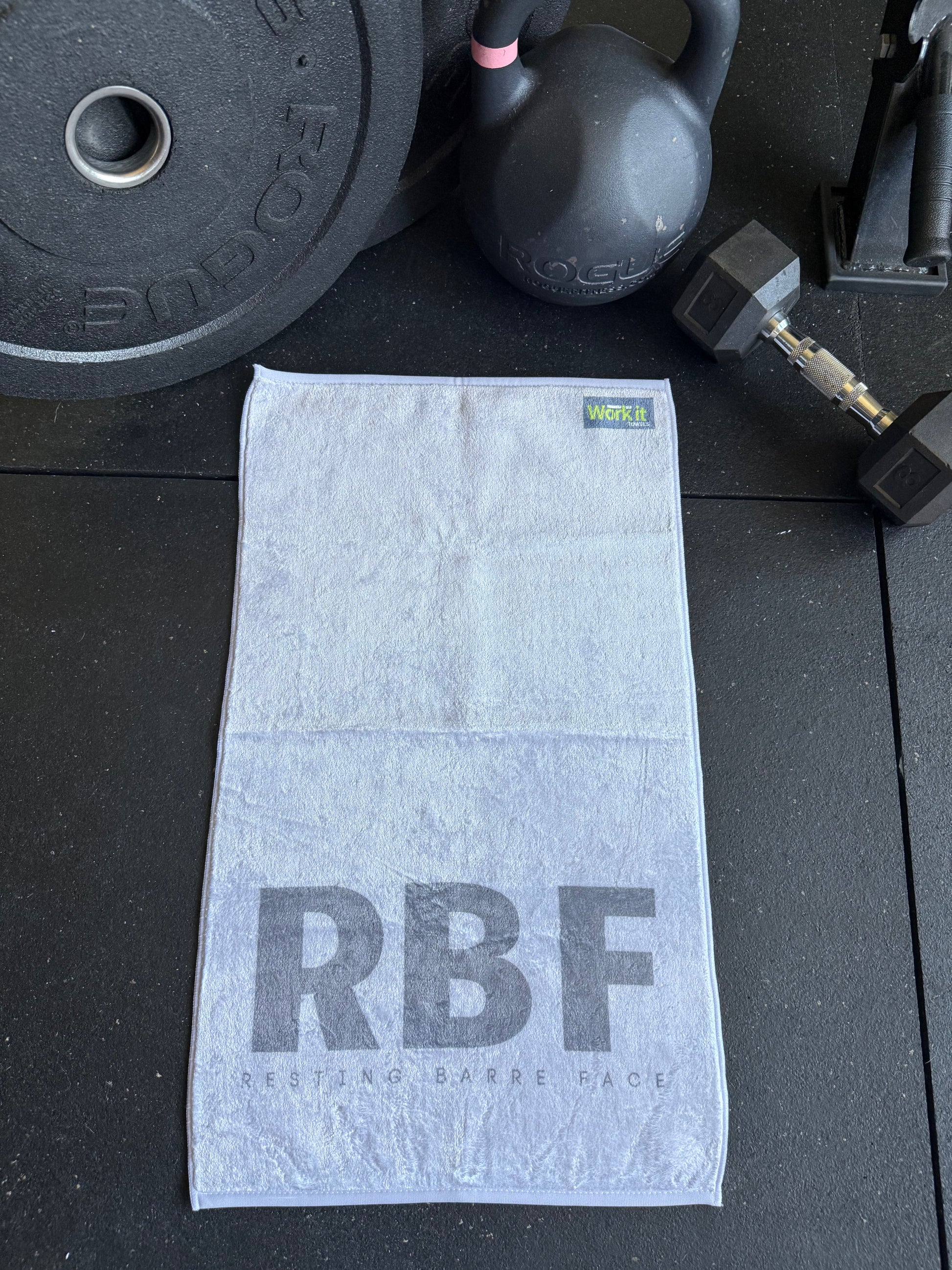 Gray towel with 'RBF' branding on a black surface with fitness equipment.