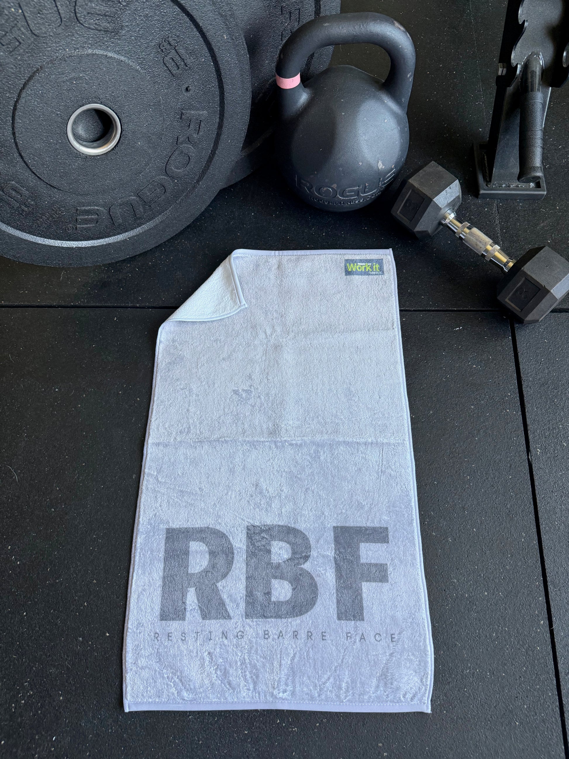Gray towel with 'RBF' branding on a black surface with fitness equipment.
