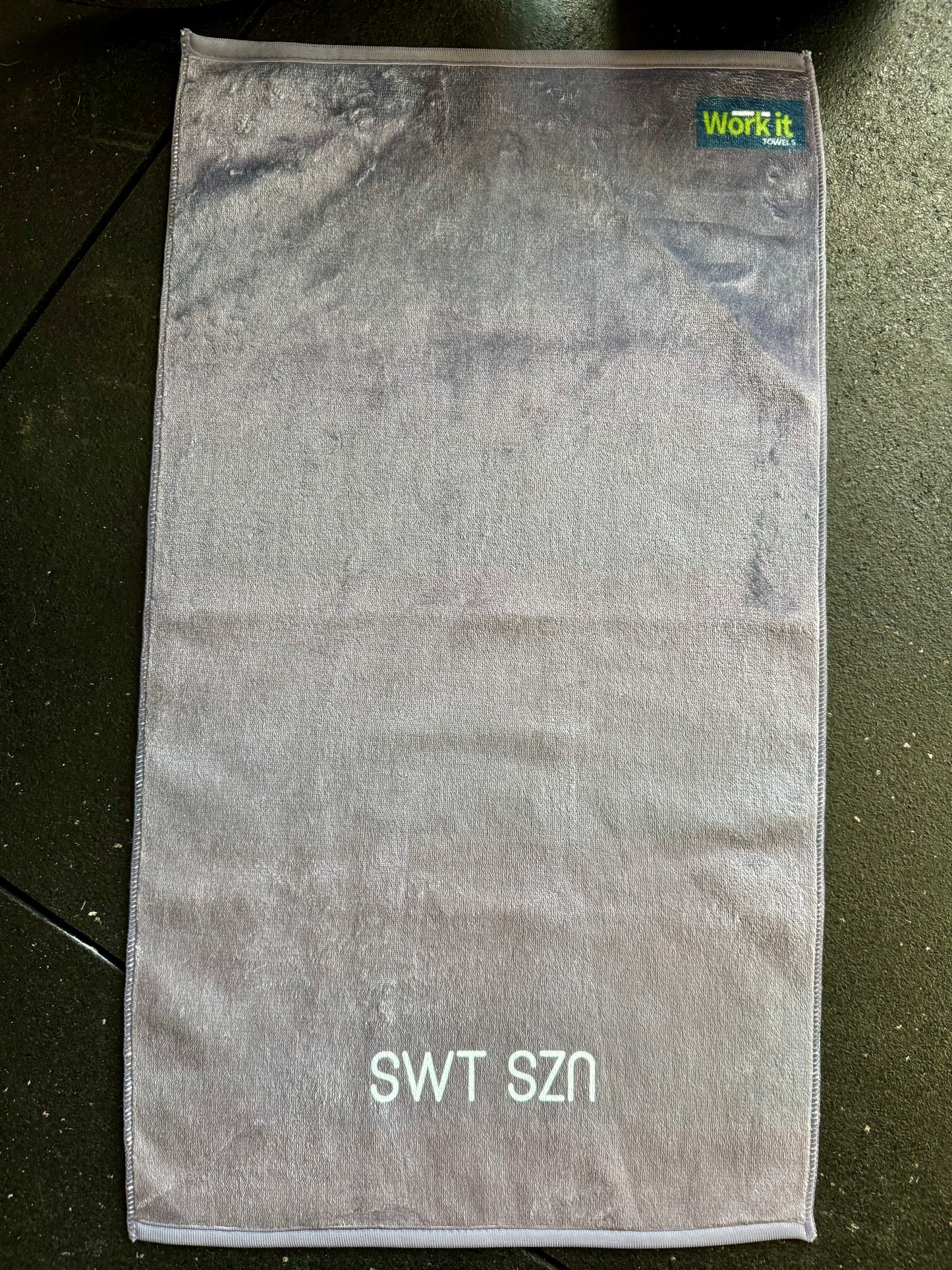 Gray towel with 'SWT SZN' text on a dark surface