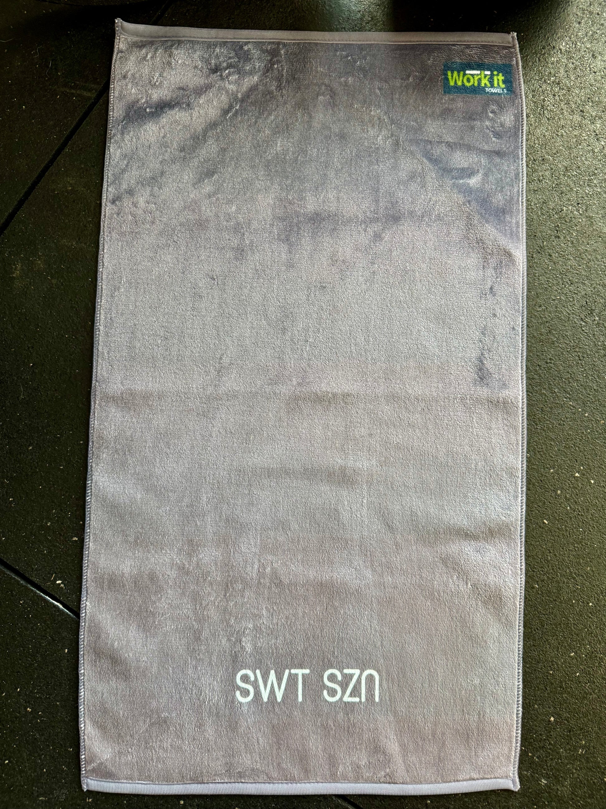 Gray towel with 'SWT SZN' text on a dark surface