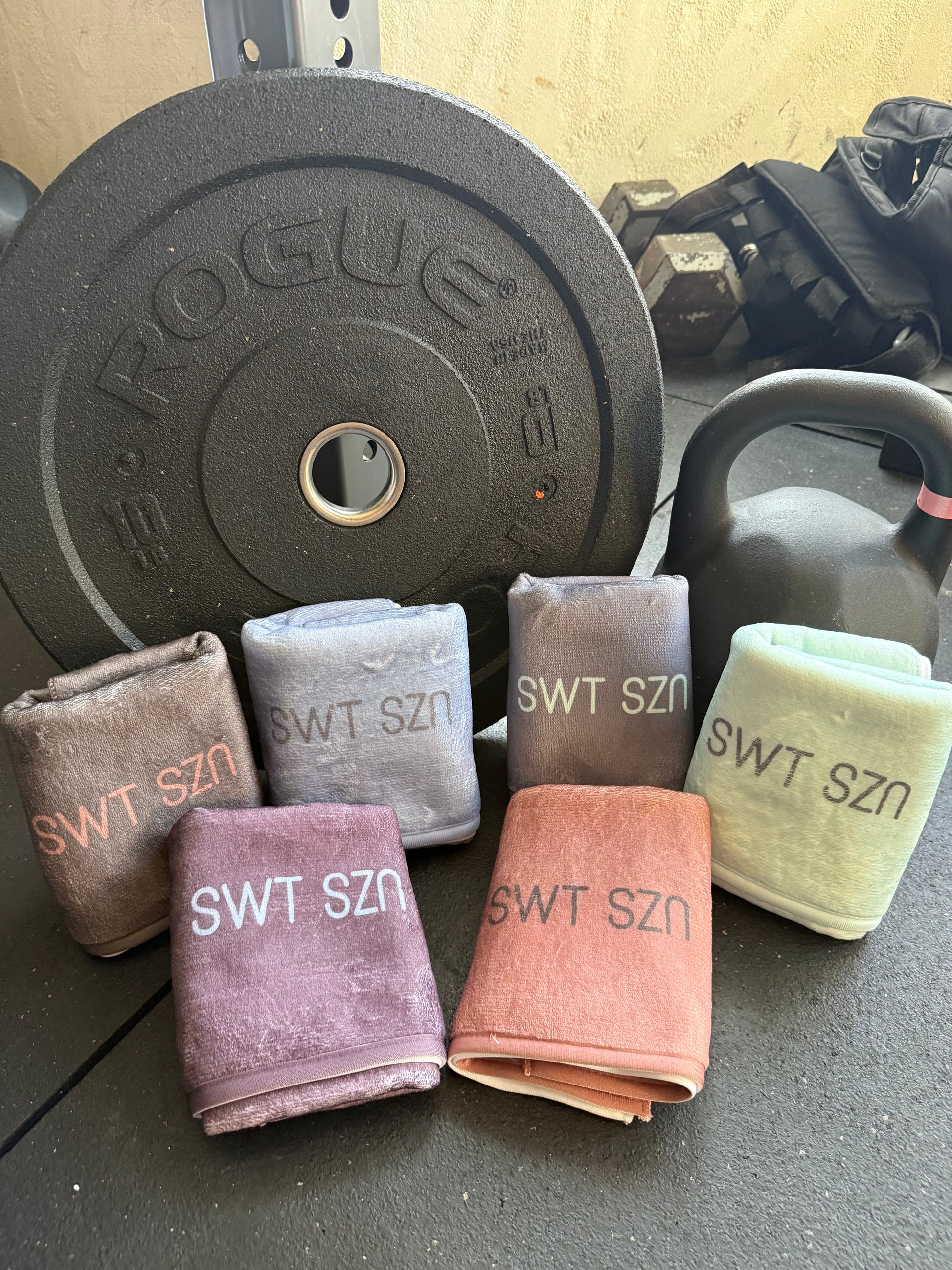 Folded towels with 'SWT SZN' branding on a gym surface with weights.
