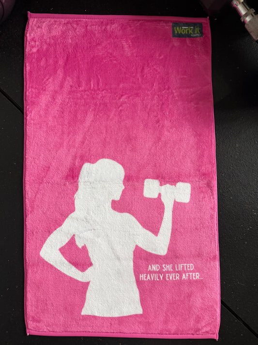 Pink towel with white silhouette of a woman lifting weights and text on a dark surface