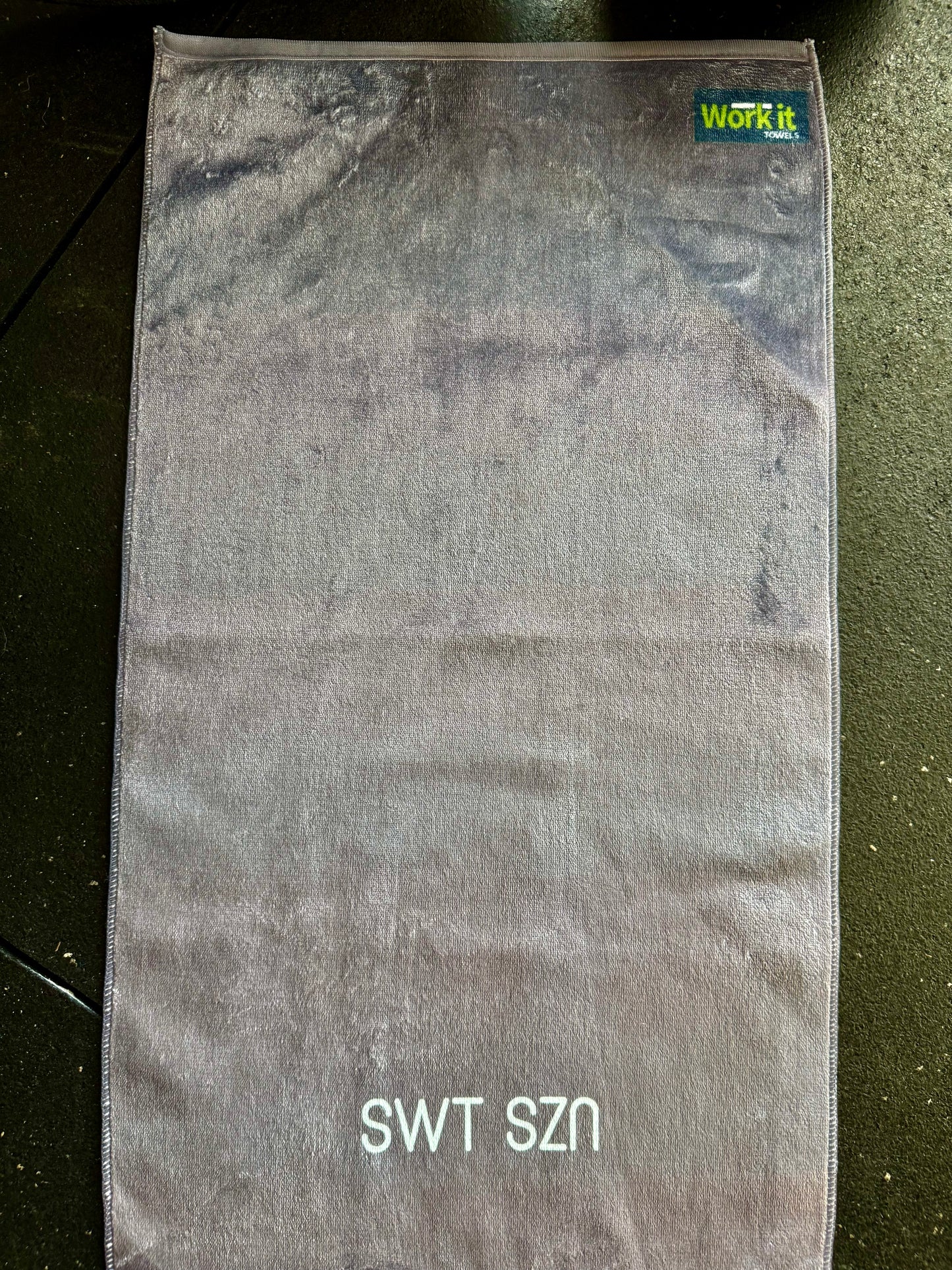 Gray towel with 'SWT SZN' text on dark gym floor 