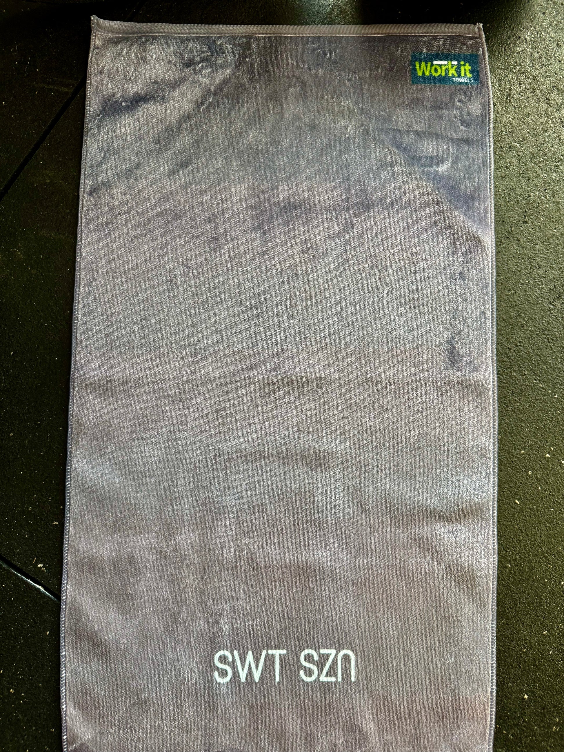 Gray towel with 'SWT SZN' text on dark gym floor 